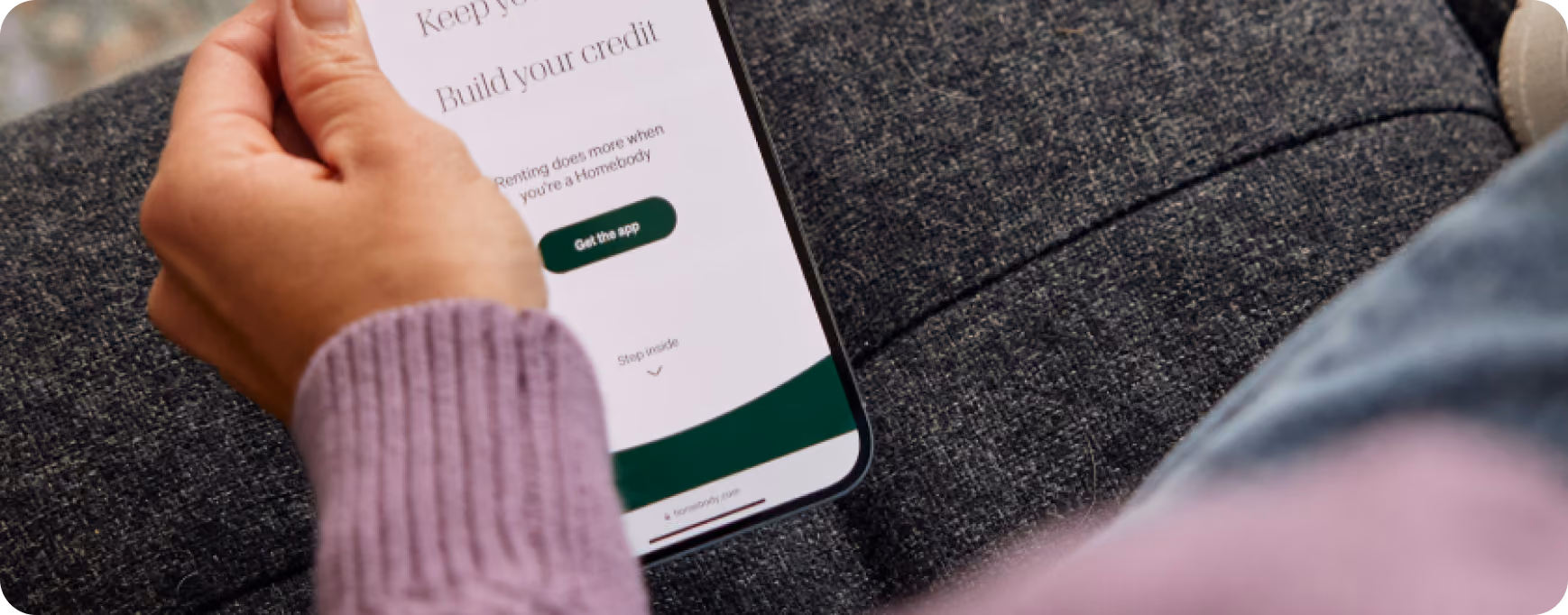 Hand holding a smartphone showing a credit-building app screen with a Get the app button
