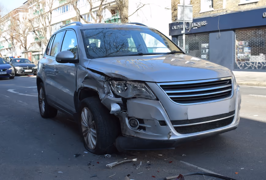 Silver SUV with severe front passenger-side crash damage and debris on an urban street