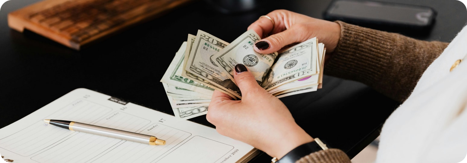 Someone counting out cash at a table with a planner open