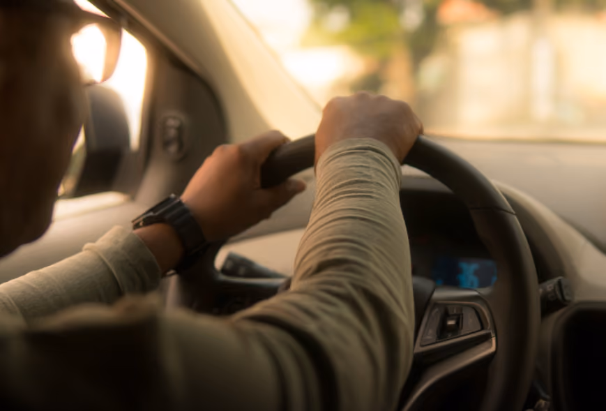 Driver’s hands on a steering wheel in warm daylight with a blurred suburban road ahead