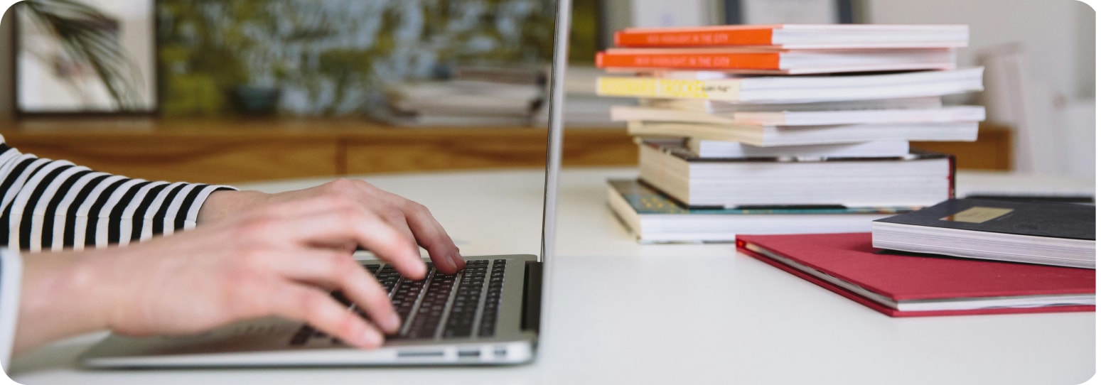 Someone typing on a laptop with books on the table