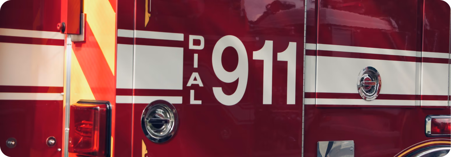 Close-up of a red emergency vehicle showing “Dial 911” text with reflective striping and a rear light.