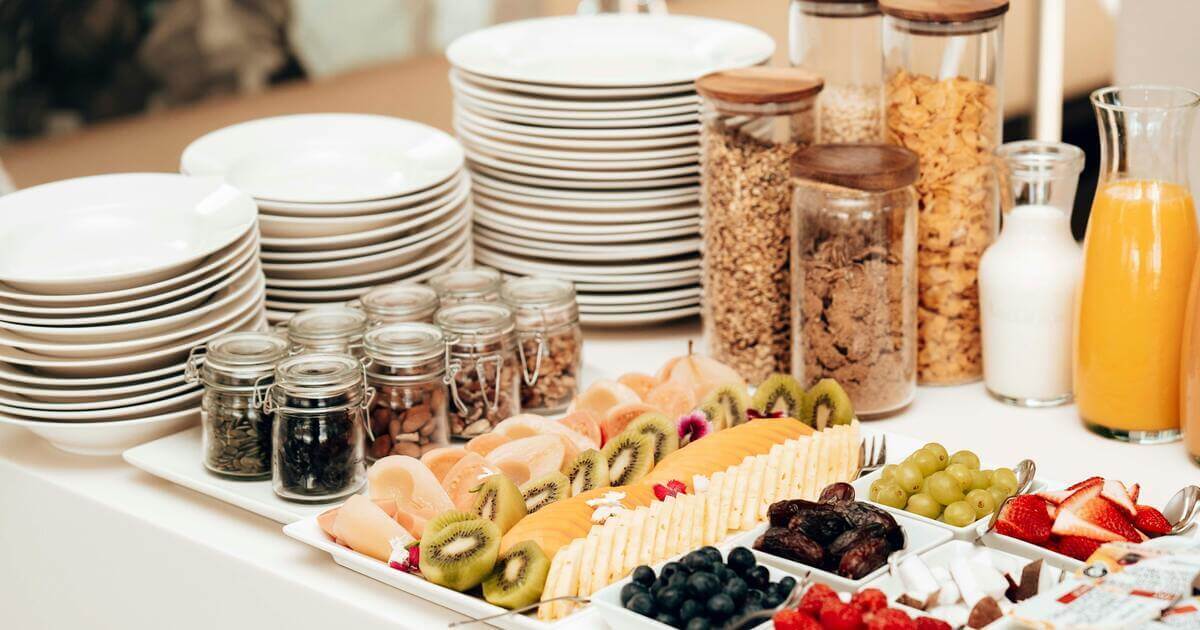 Close-up of a fresh breakfast buffet for a resident appreciation event, featuring sliced fruit, yogurt toppings in glass jars, fresh berries, and orange juice.