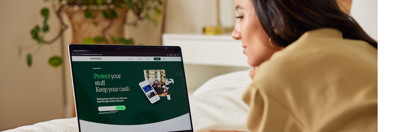 A lady laying on a bed in her bedroom looking at a computer with website on it