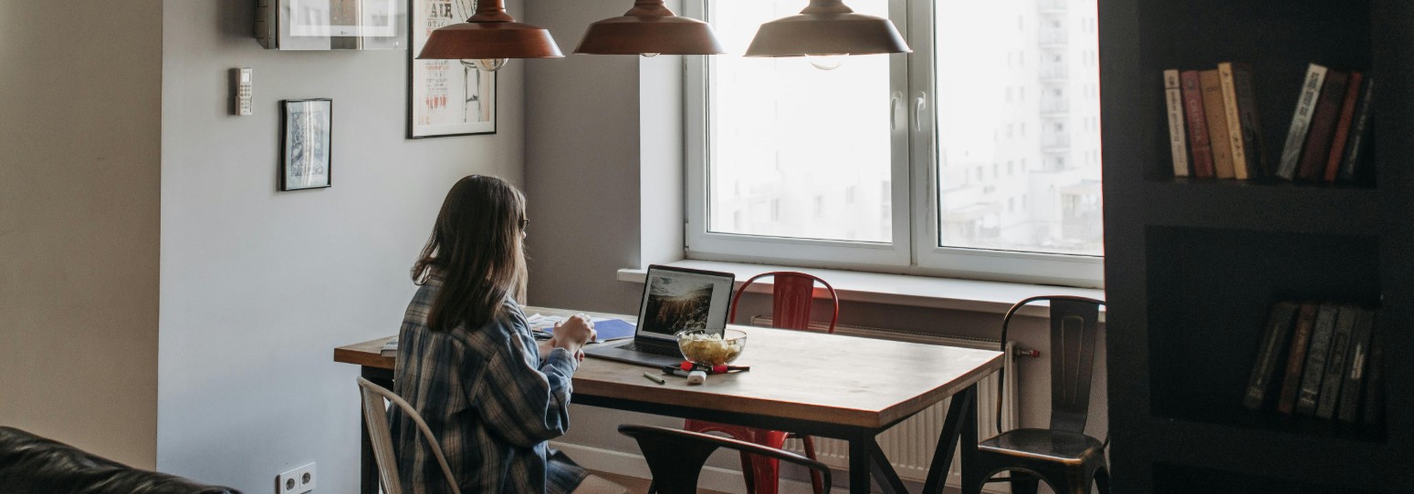 A person sitting at a dining room table on their computer