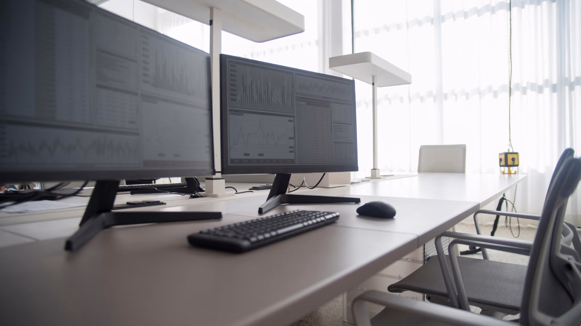 Office desk setup with computer monitors displaying analytics dashboards and data charts.