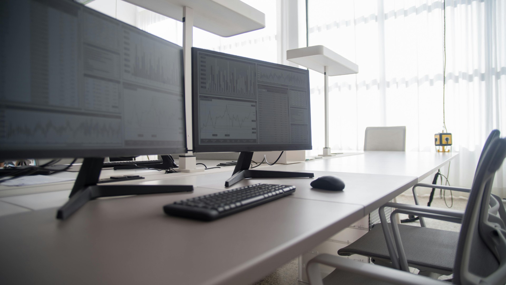 Office desk setup with computer monitors displaying analytics dashboards and data charts.