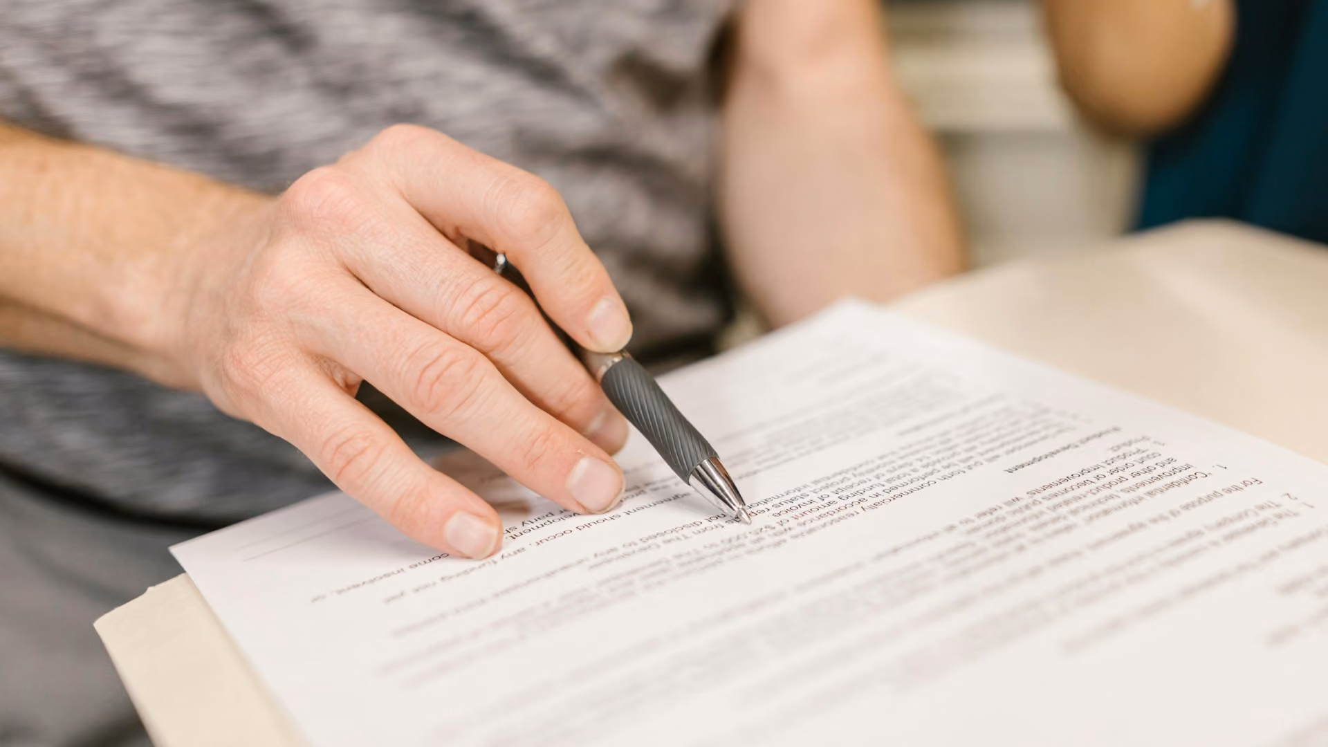 Person reviewing and signing lease paperwork with a pen during a rental agreement meeting.