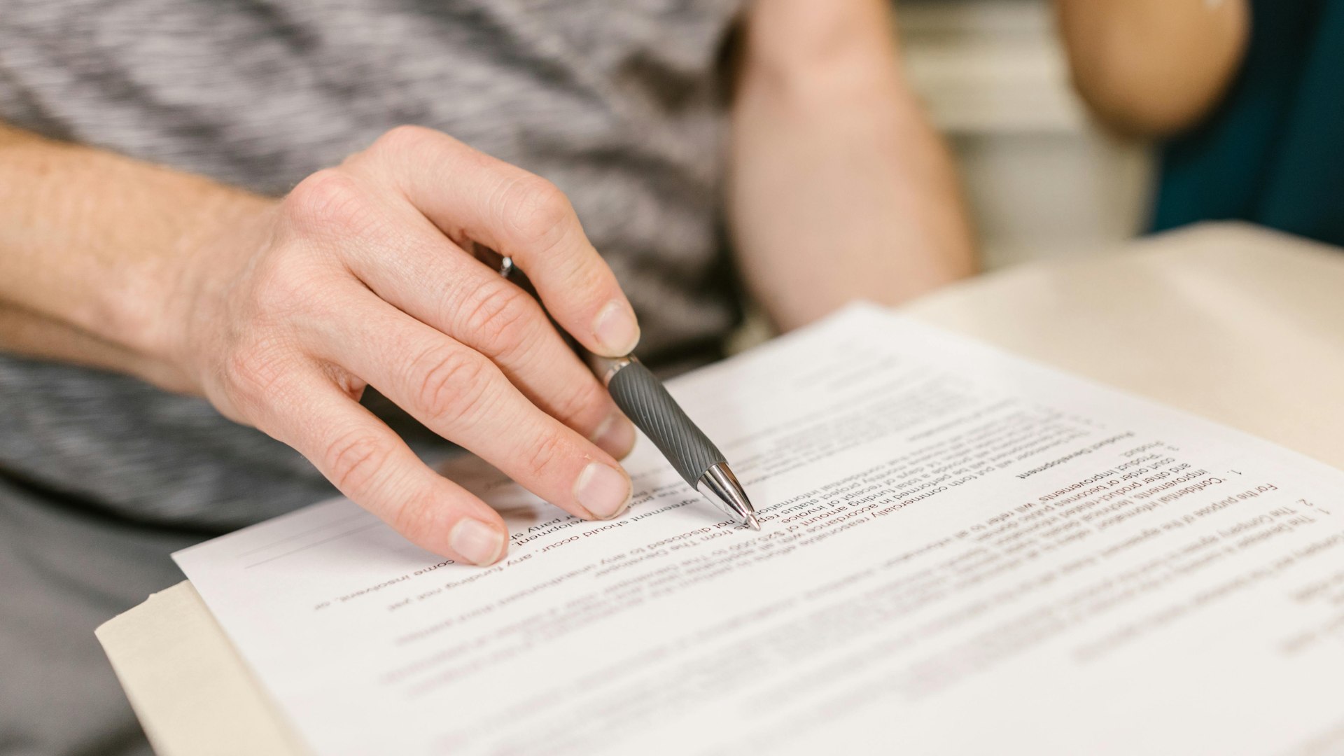 Person reviewing and signing lease paperwork with a pen during a rental agreement meeting.