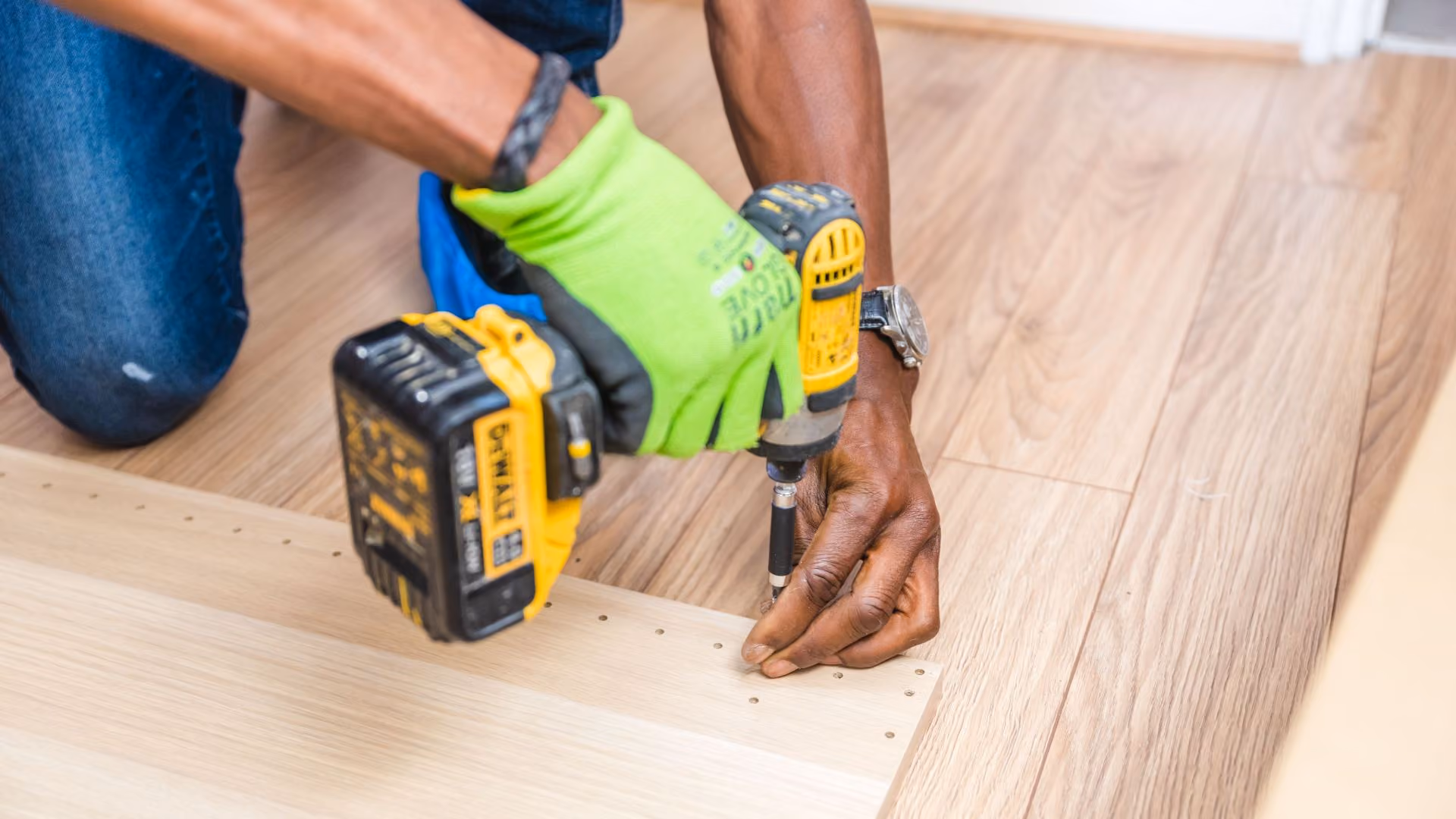 Person using a power drill to assemble flooring materials during a home improvement project.
