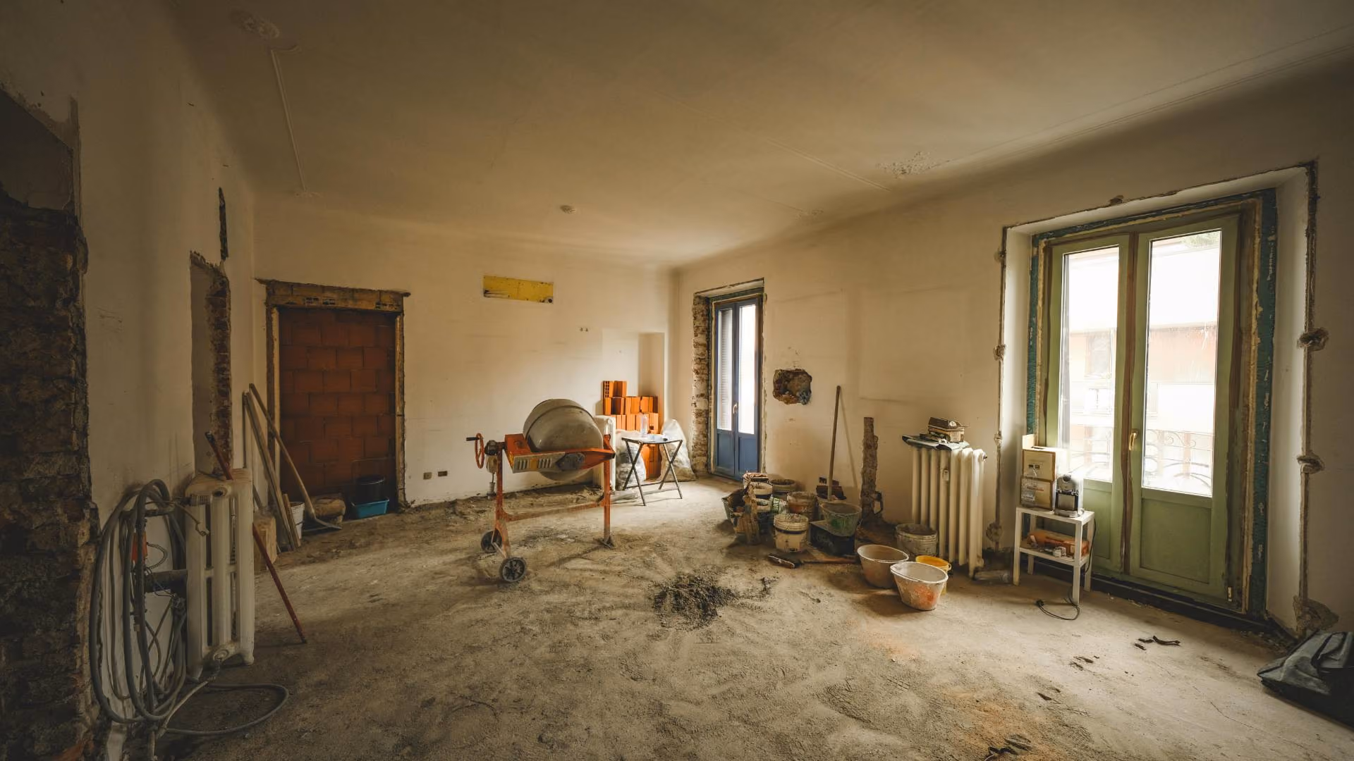 Apartment interior under renovation with construction tools, exposed walls, and building materials spread throughout the room.