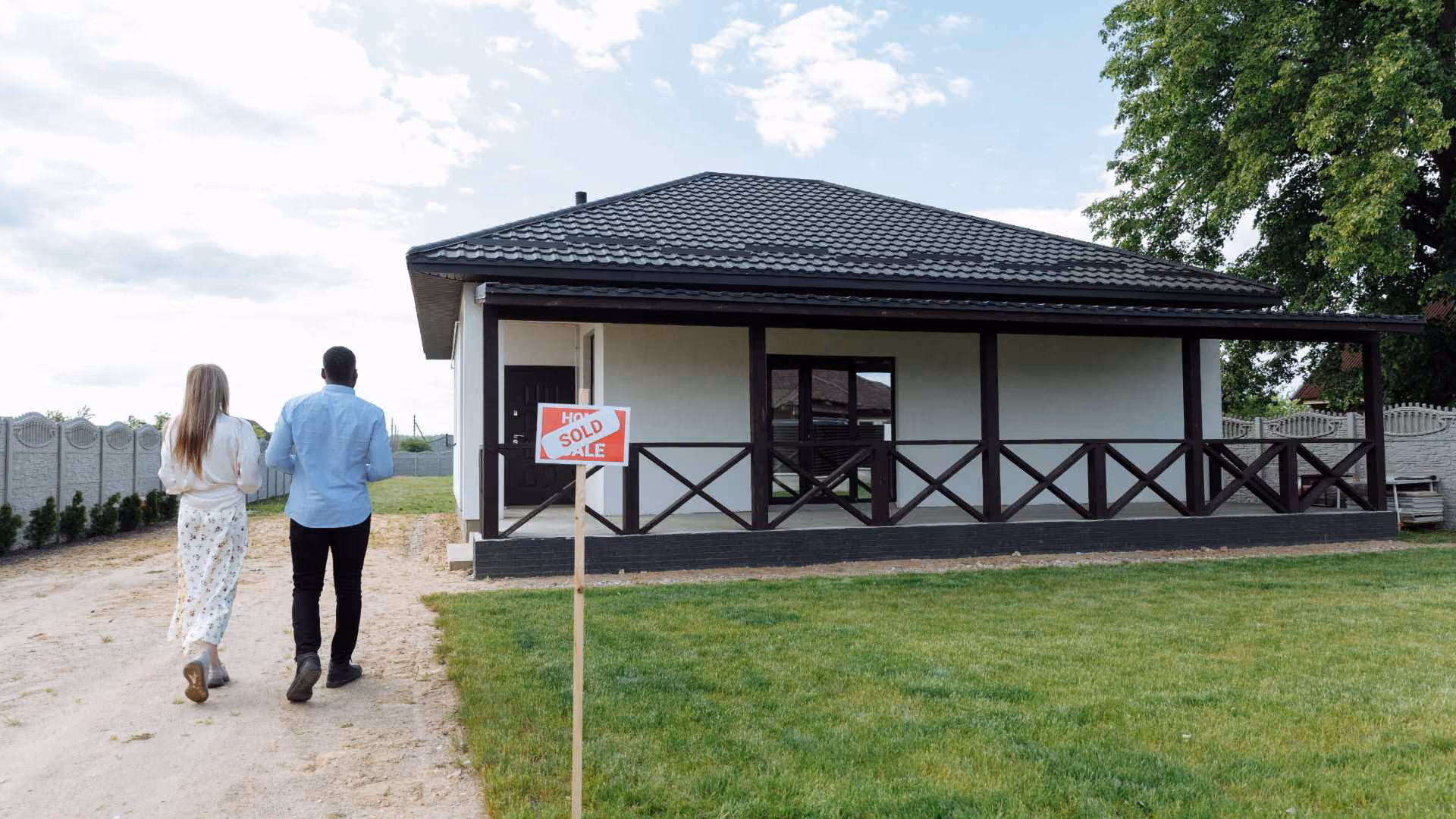 Couple walking toward a newly purchased home with a sold sign displayed in the front yard.