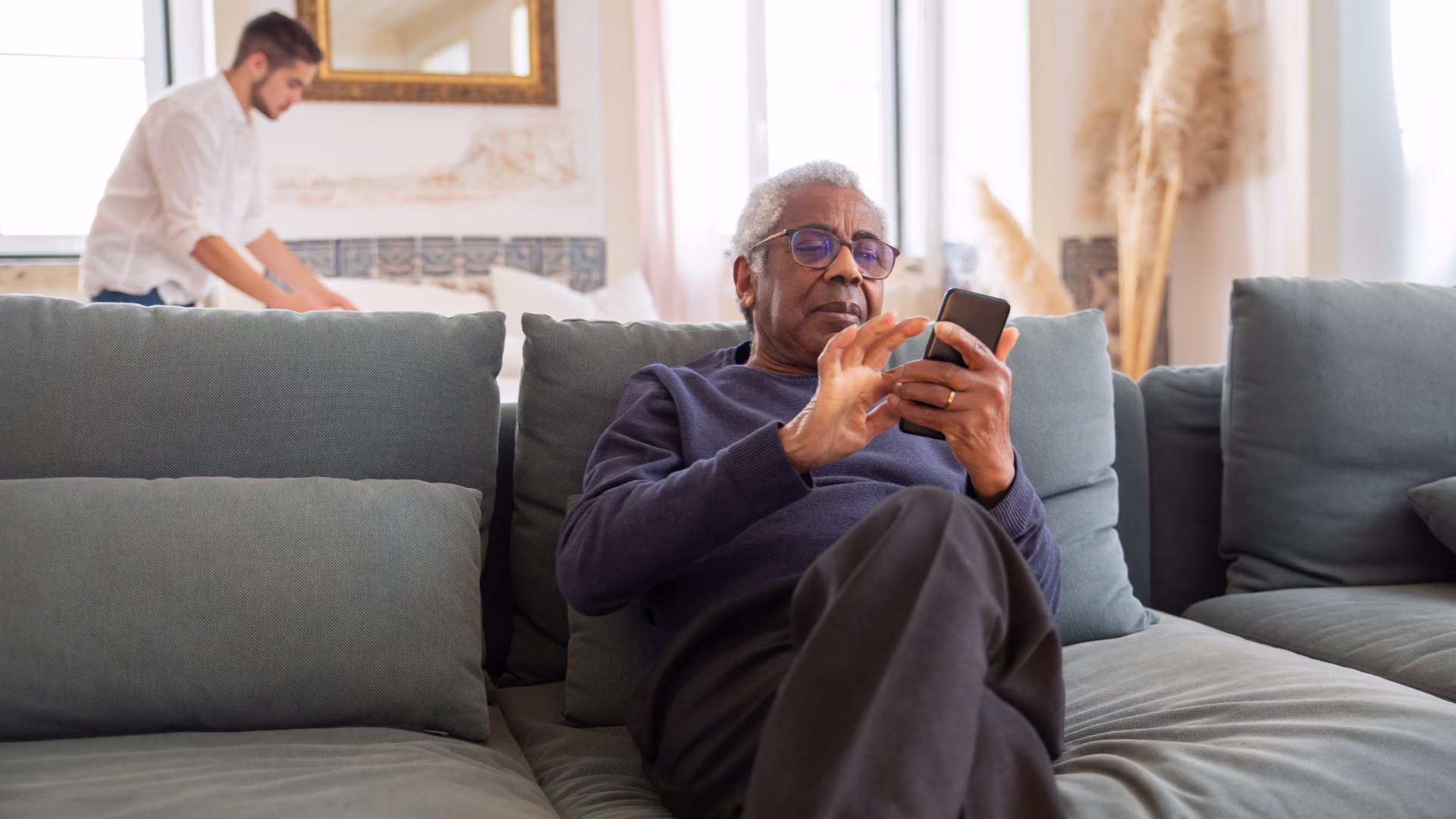 An older person sitting on a couch looking at their smartphone