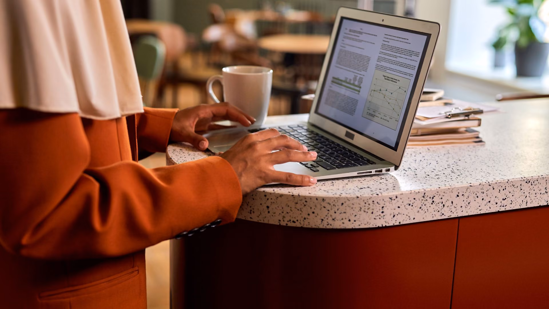 Person working on a laptop at a kitchen counter with a coffee cup nearby