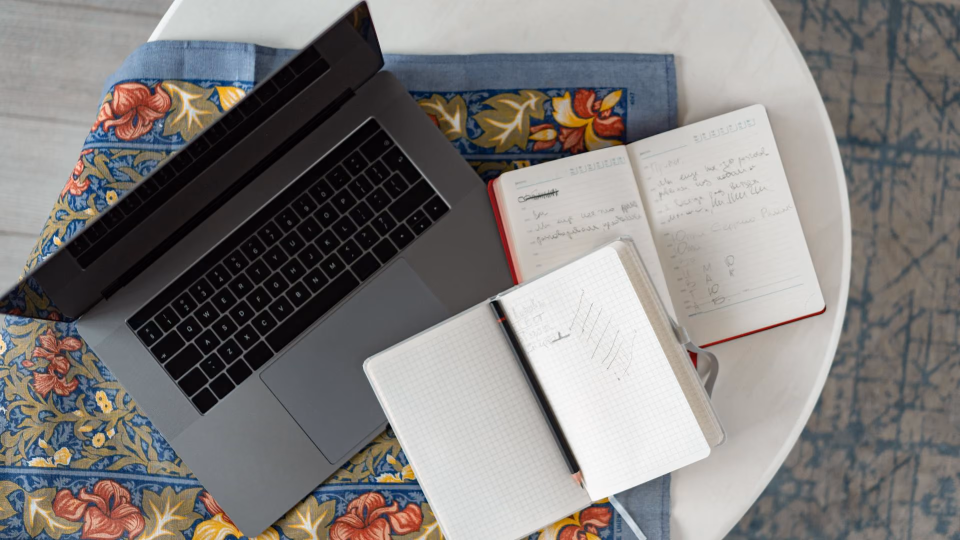 Overhead view of a laptop and open notebooks with handwritten notes on a round table