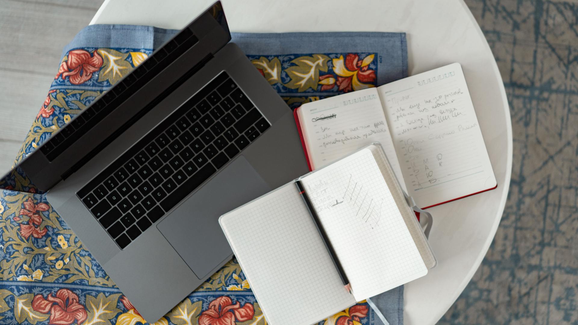 Overhead view of a laptop and open notebooks with handwritten notes on a round table