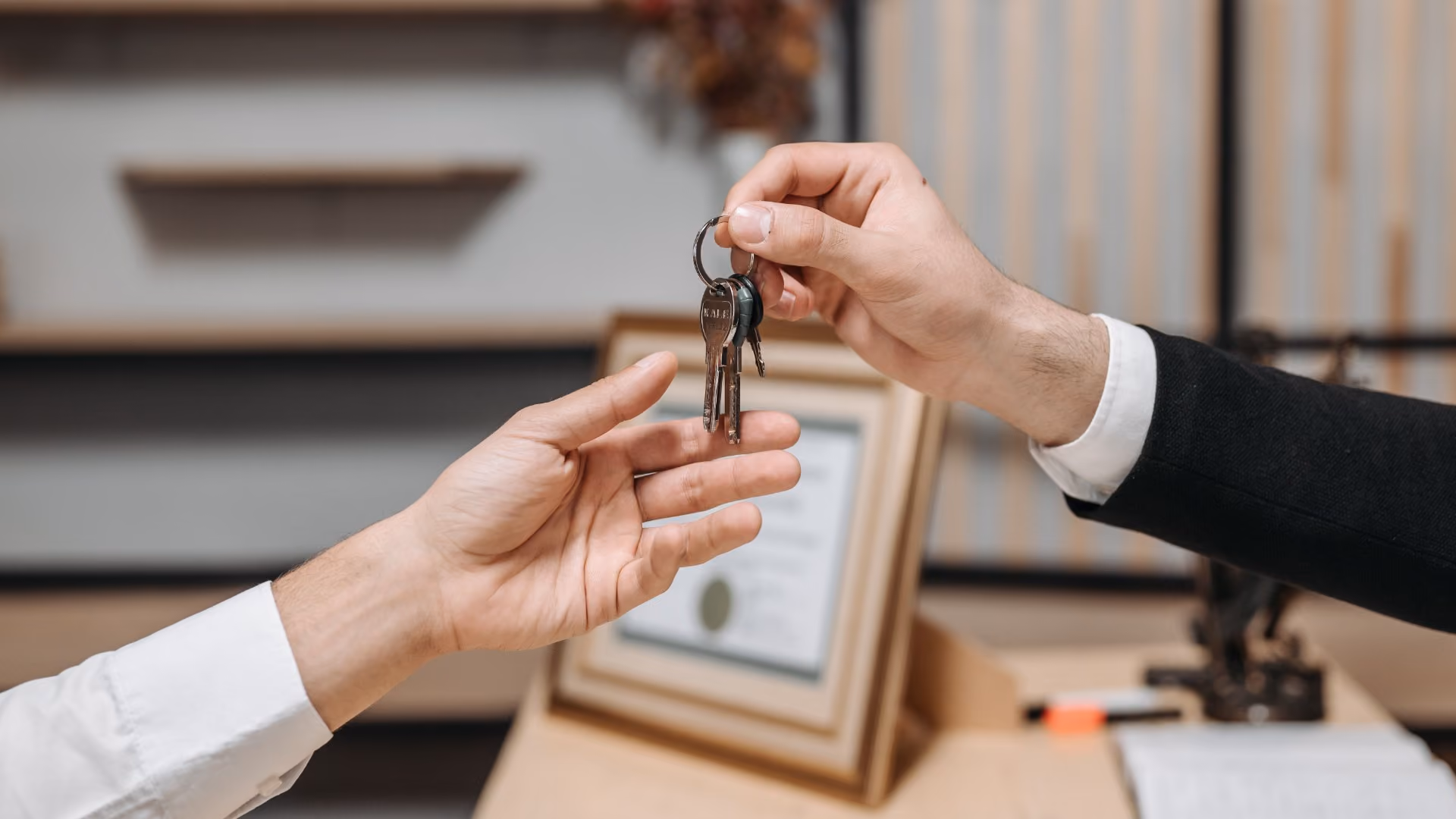 Person handing a set of keys to another person across a desk