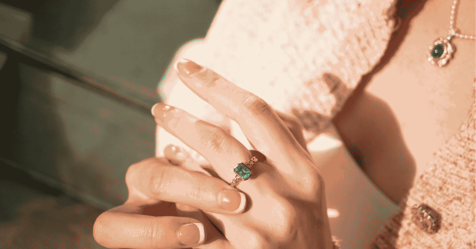woman's hands with an emerald ring on a finger and pearl necklace in the foreground