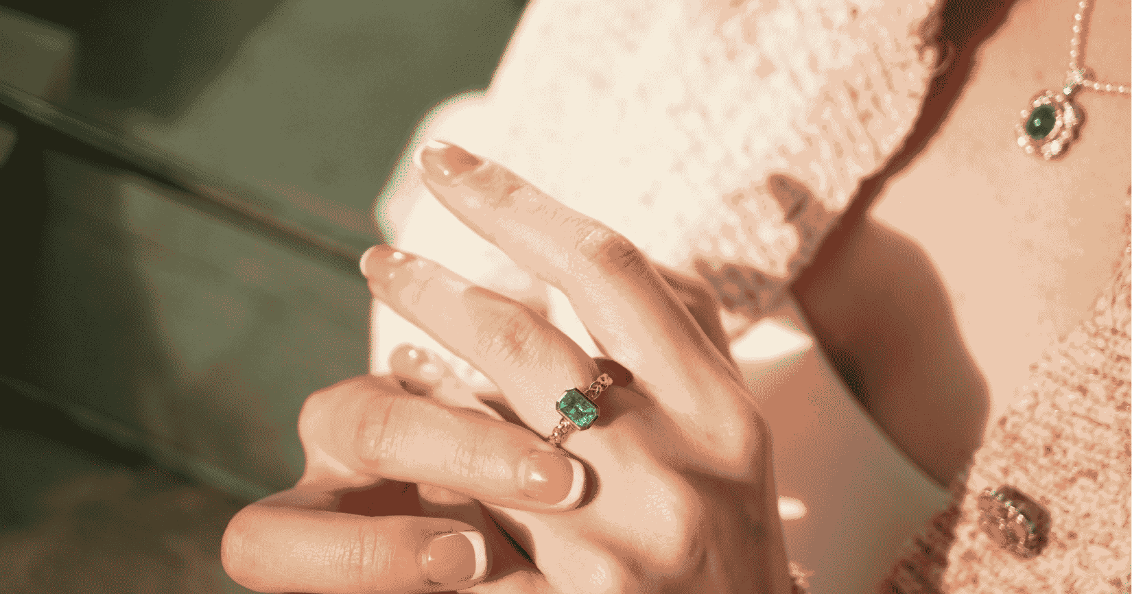 woman's hands with an emerald ring on a finger and pearl necklace in the foreground