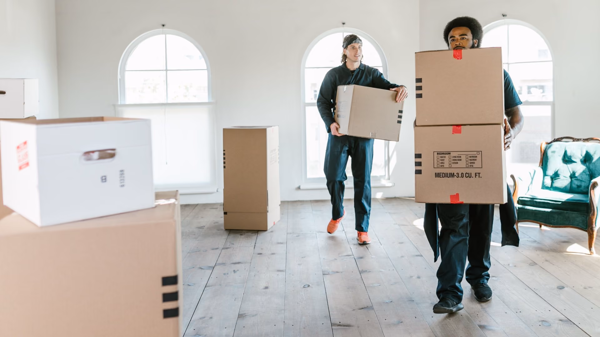 Two people carrying moving boxes into a new apartment.