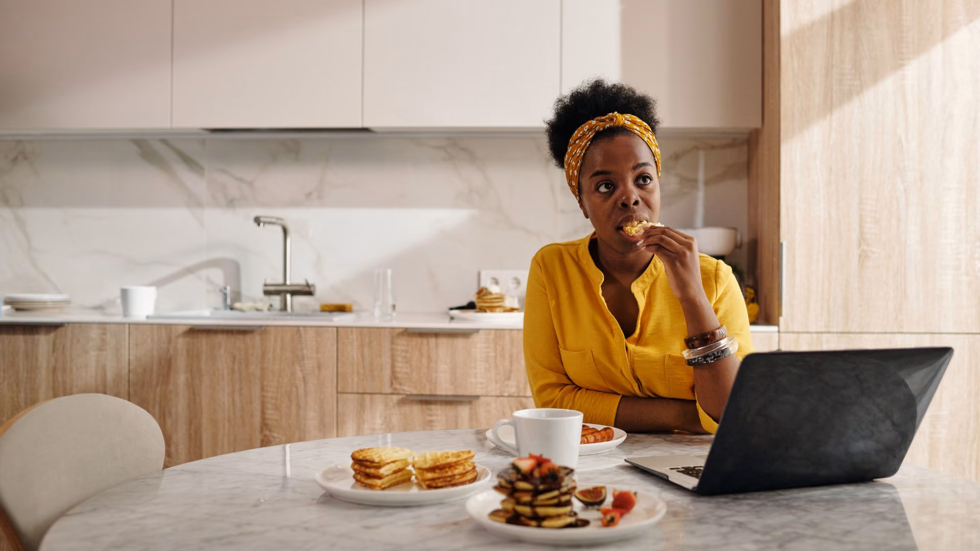 Person using a laptop while having breakfast in a modern apartment kitchen.