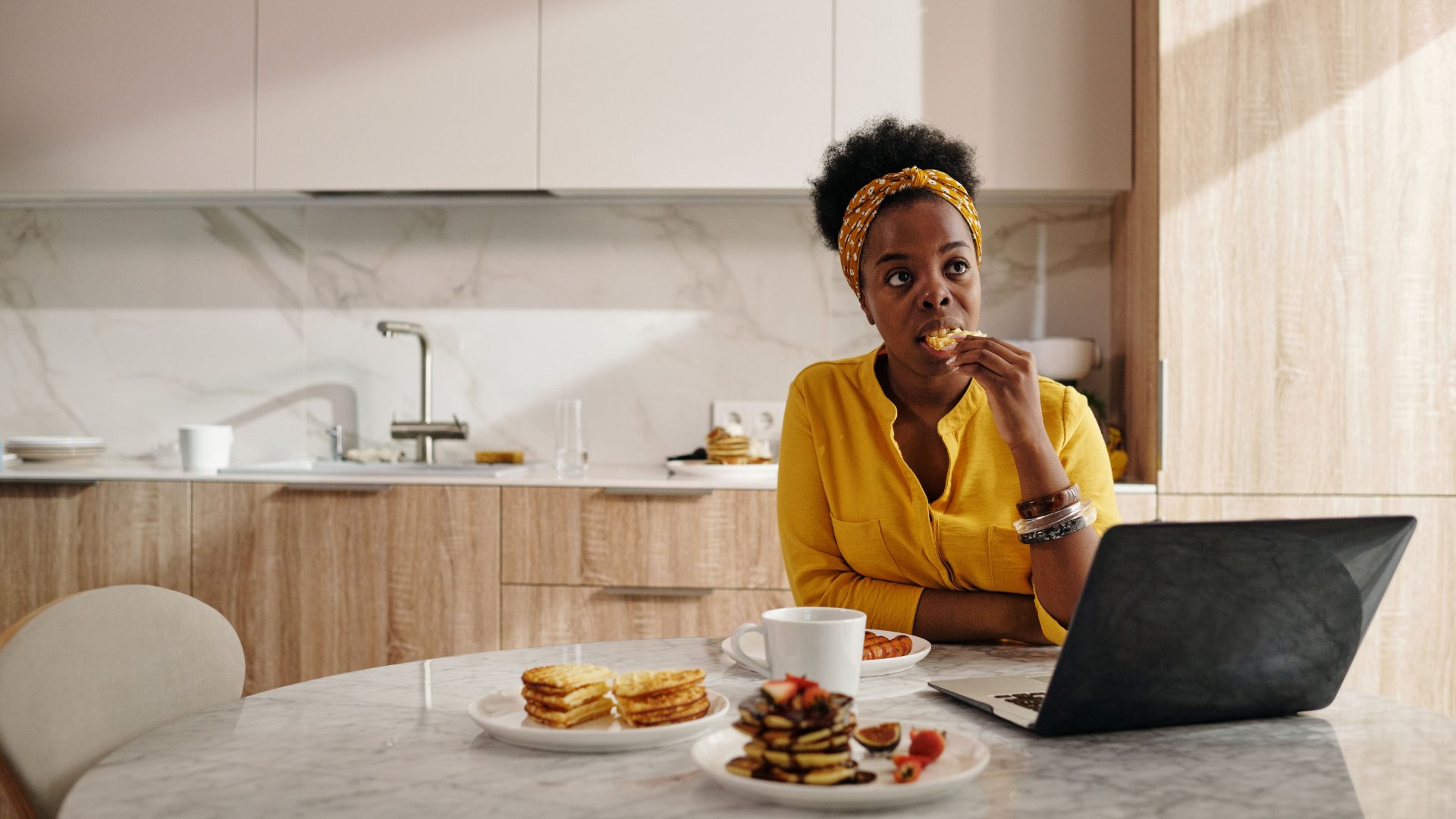 Person using a laptop while having breakfast in a modern apartment kitchen.