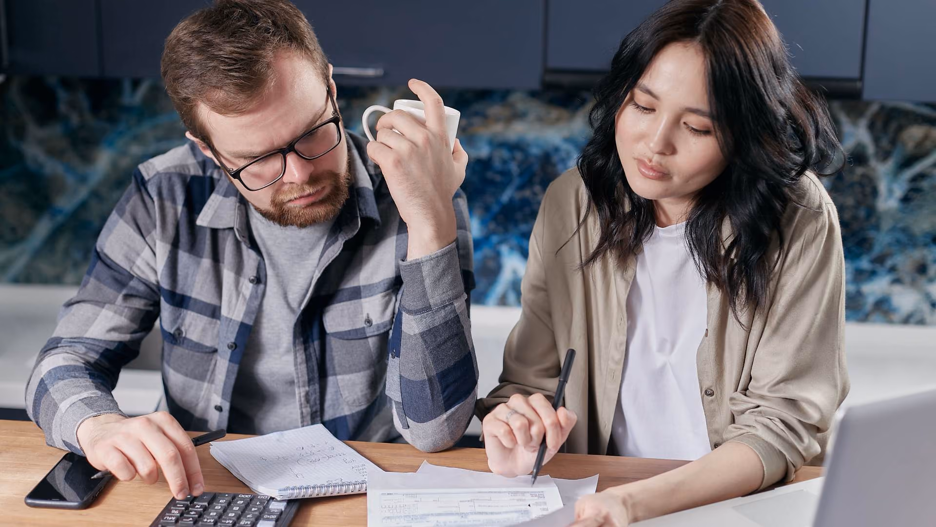 Person using a calculator and laptop to create a monthly household budget.
