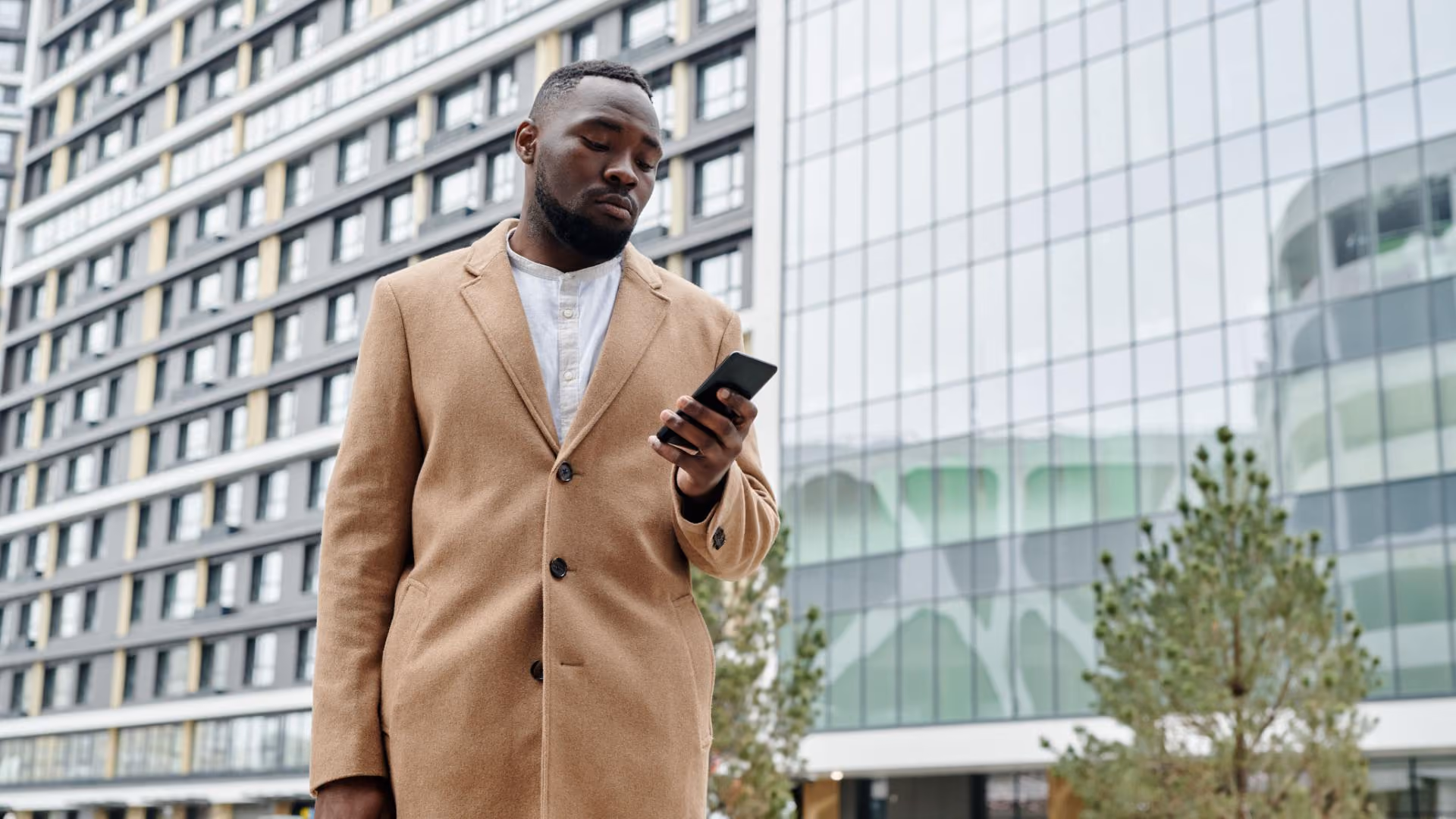 Person looking at a smartphone outside a modern apartment building.