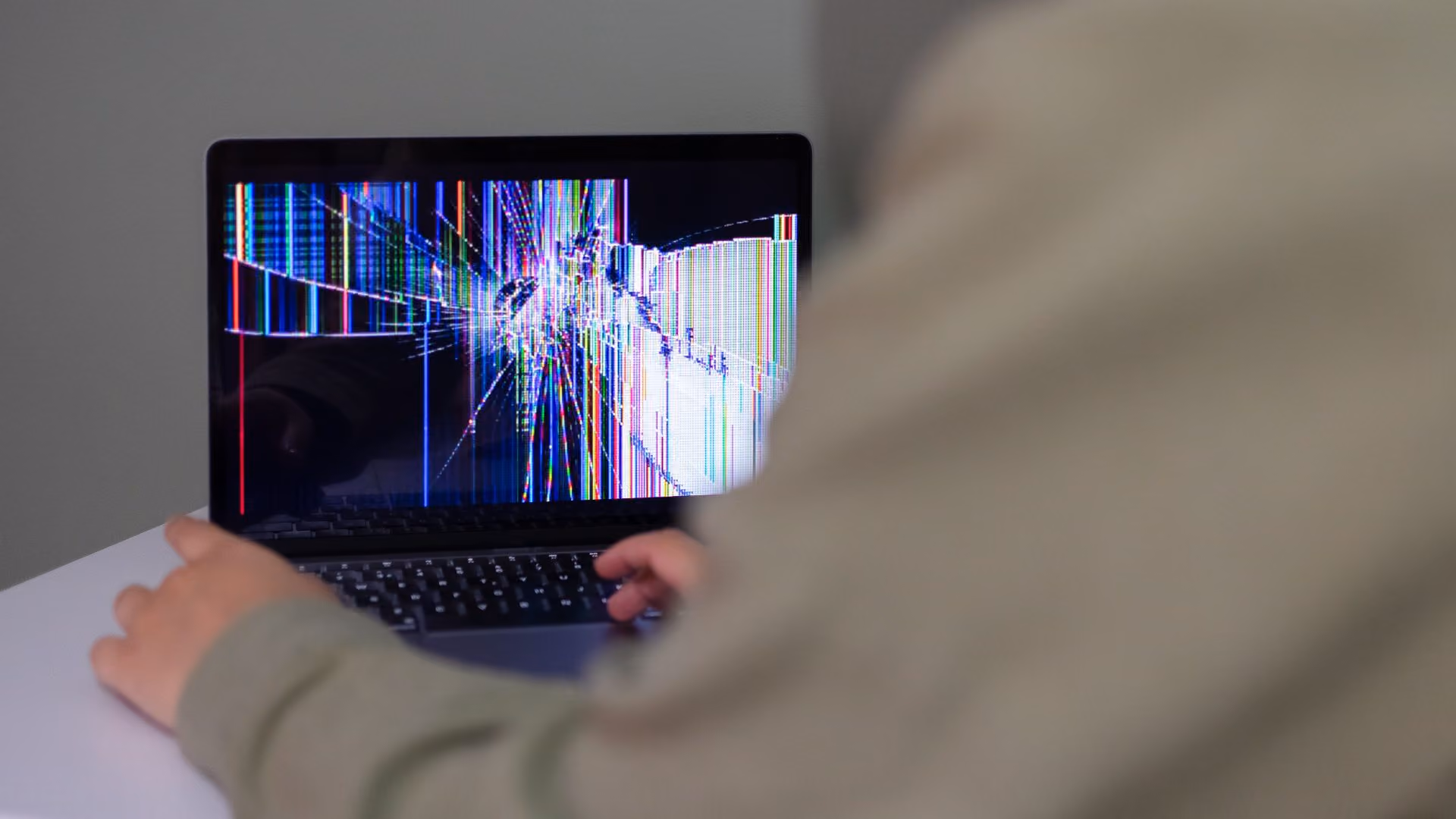 Person using a laptop with a damaged display showing colorful screen distortion.