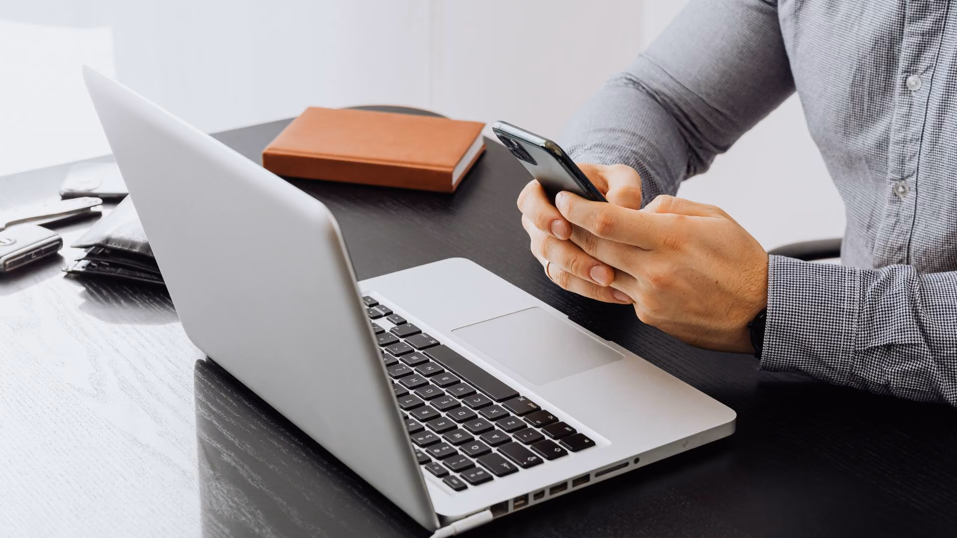 Person using a smartphone next to a laptop on a desk.
