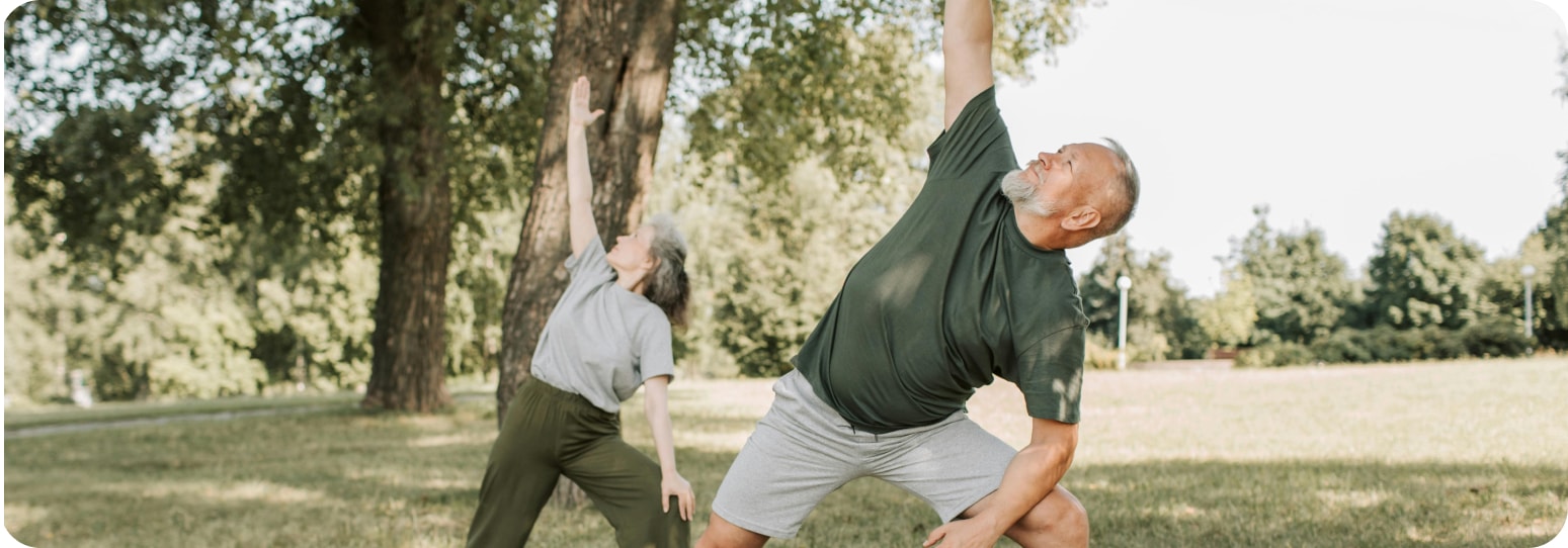 Older man and woman doing an outdoor stretching routine together in a park