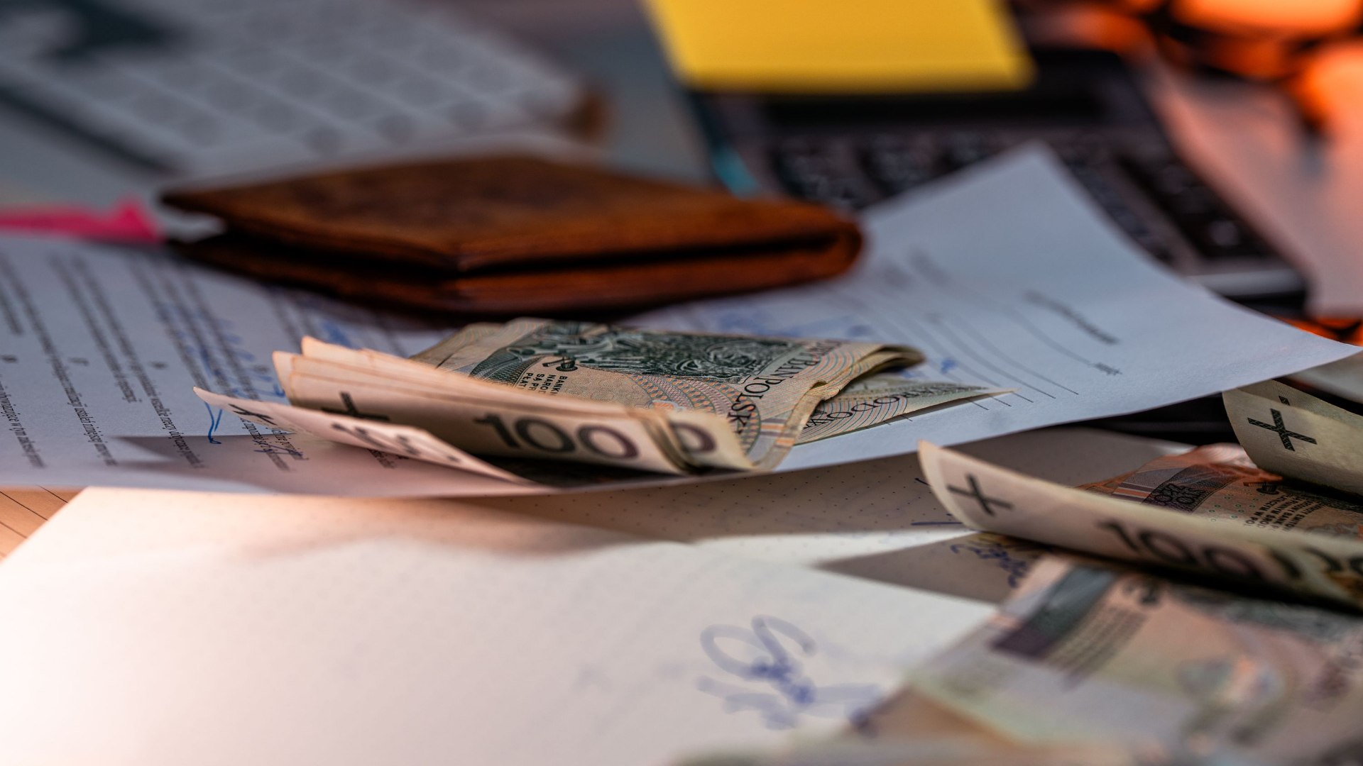 Polish banknotes scattered across financial documents beside a wallet and calculator.