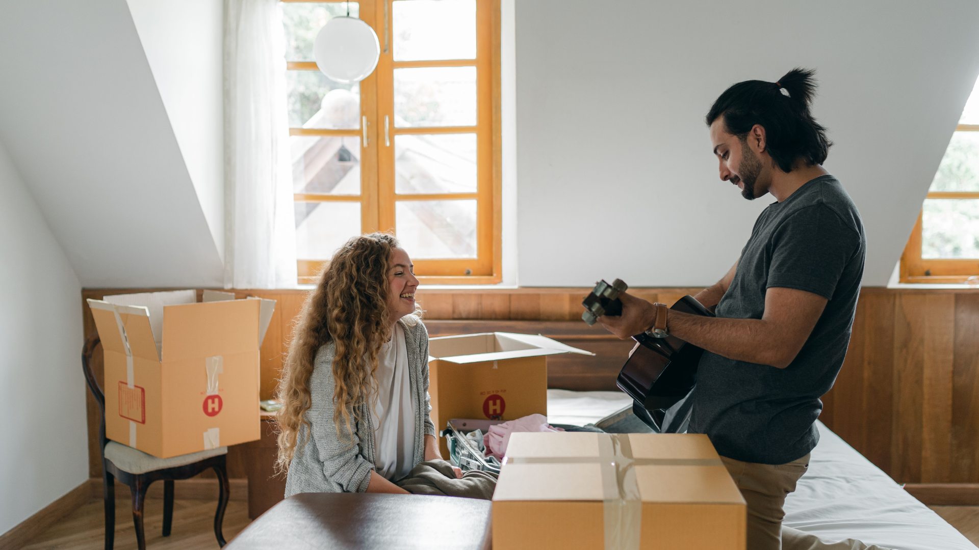 Couple unpacking moving boxes together in a bright bedroom.