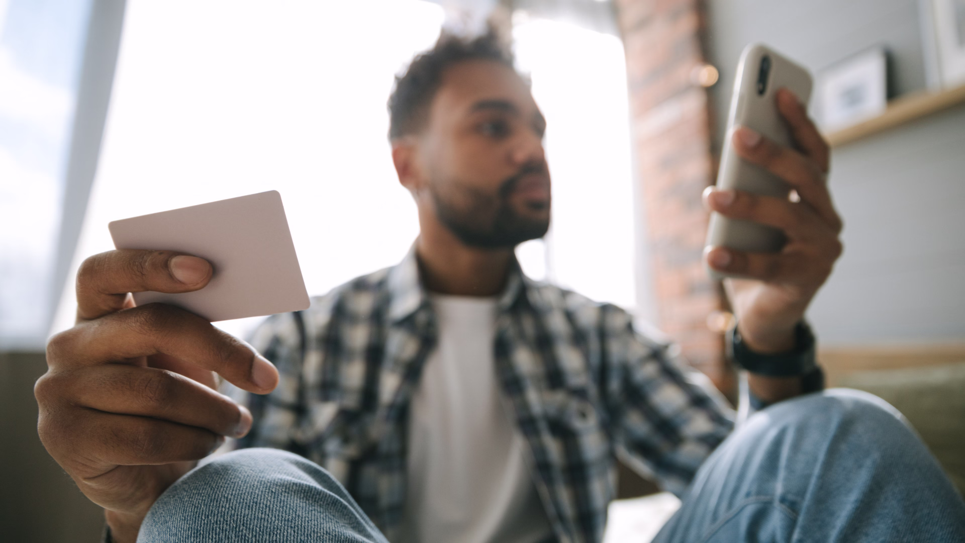 A person sitting down looking at their phone and a credit card