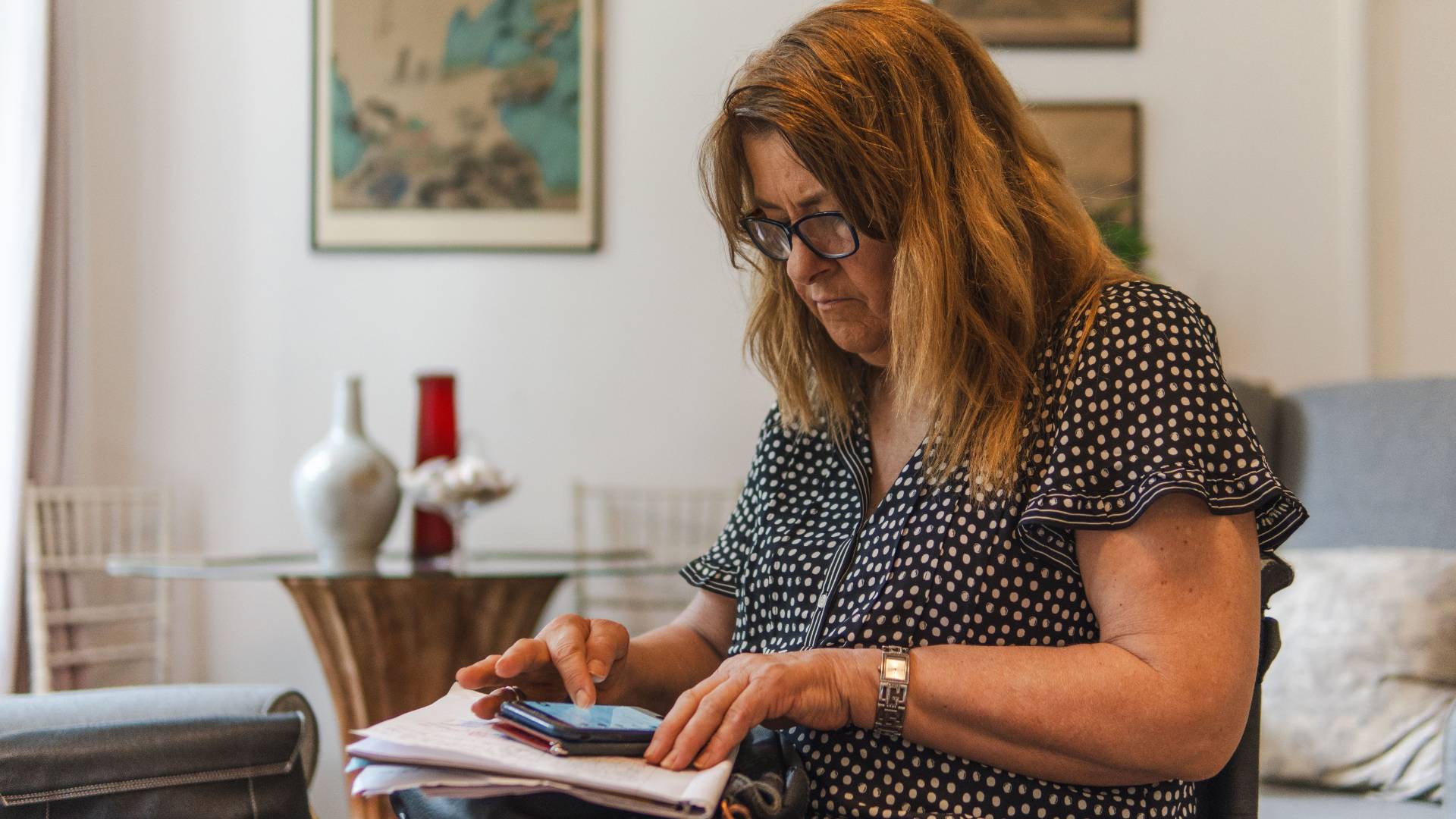 Woman reviewing paperwork and checking her phone at home