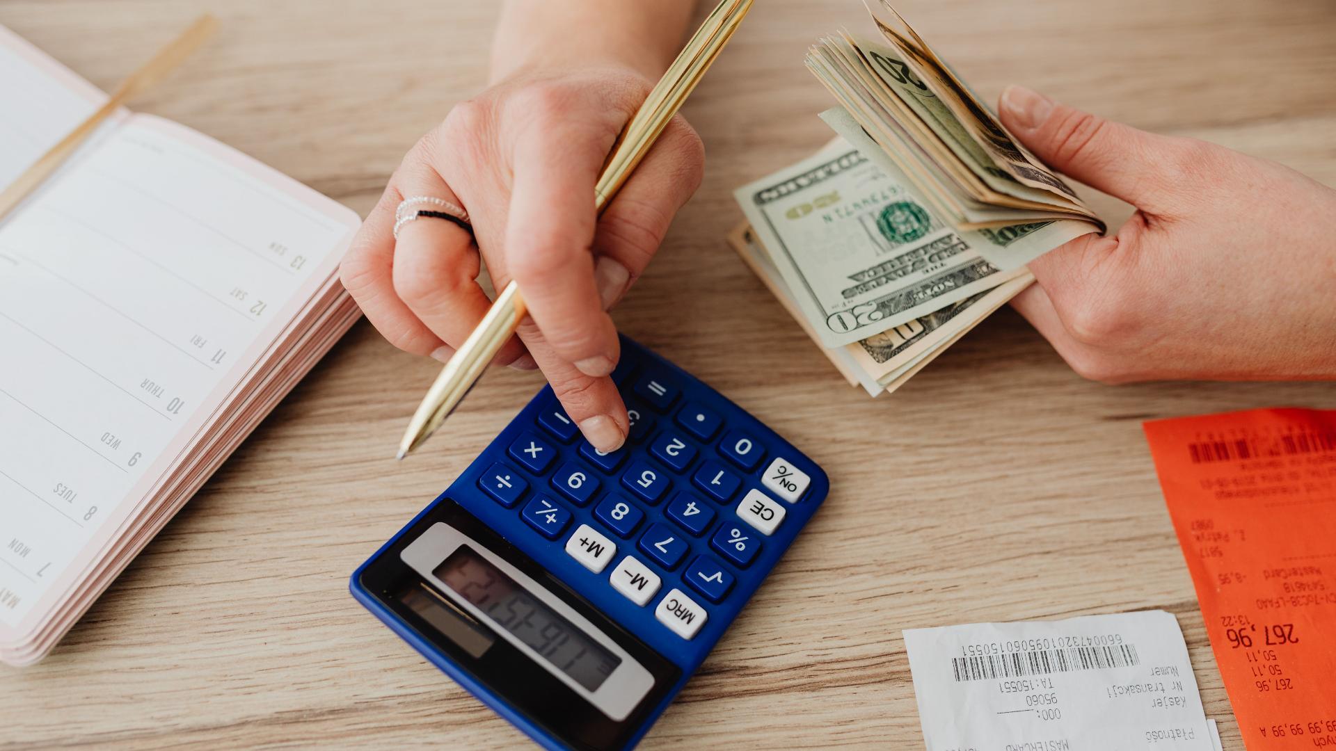 Person using a calculator while holding cash.