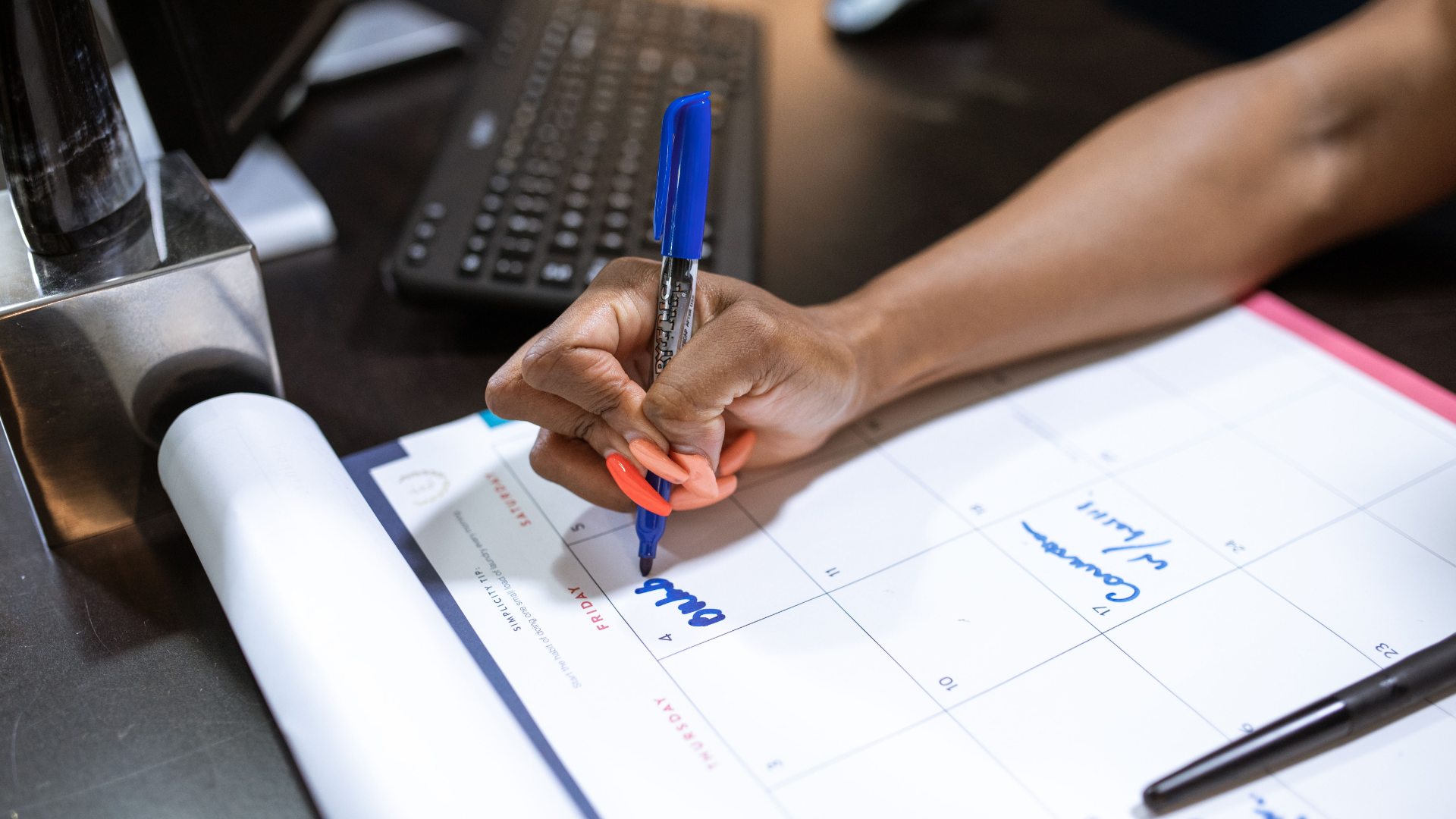 Close-up of a person writing on a desk calendar with a blue marker.