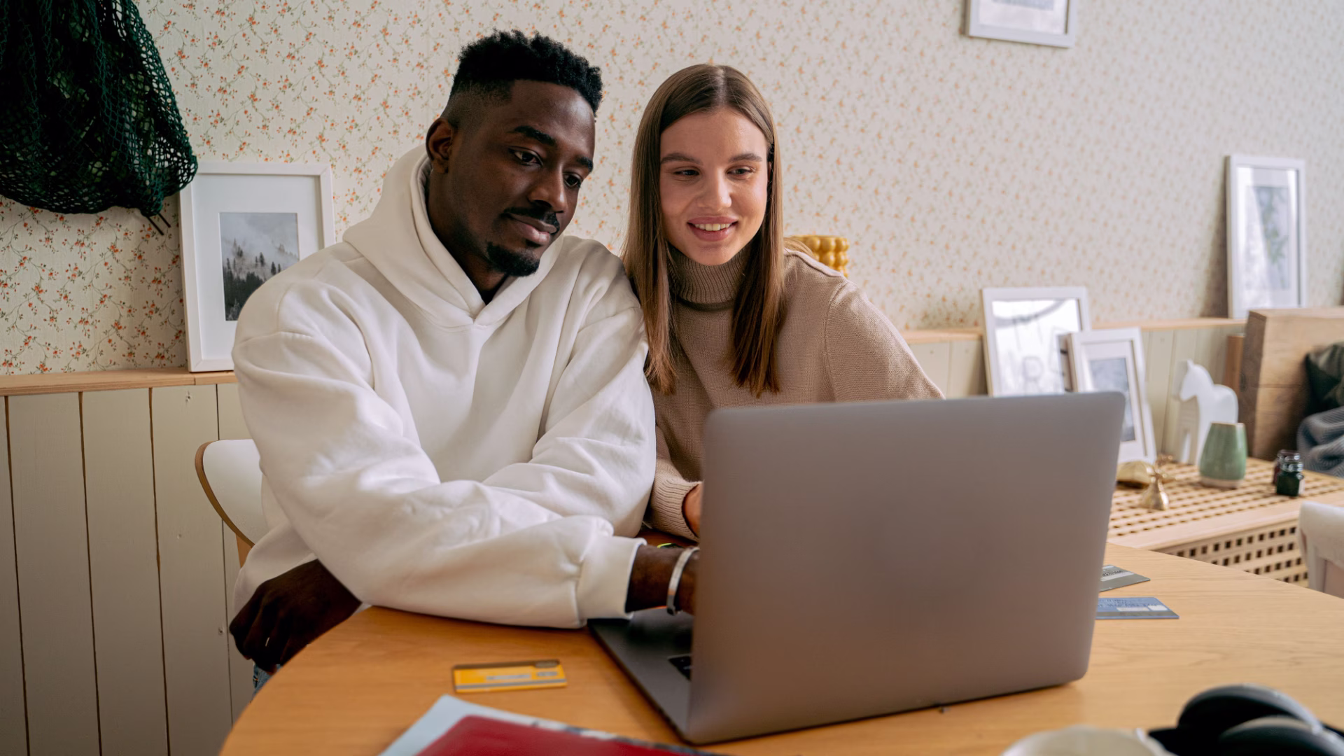 A young couple sitting at a table looking at their laptop with documents and credit cards beside them