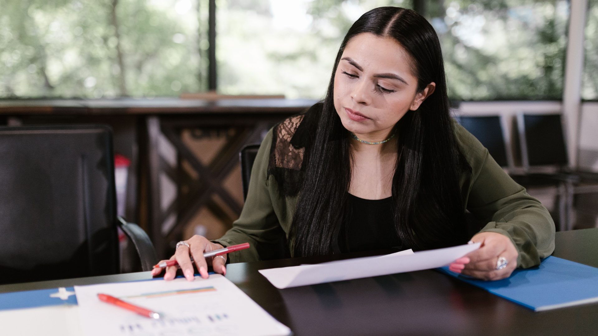 A woman seated at a desk holding a pen and carefully reviewing printed financial documents and an application.