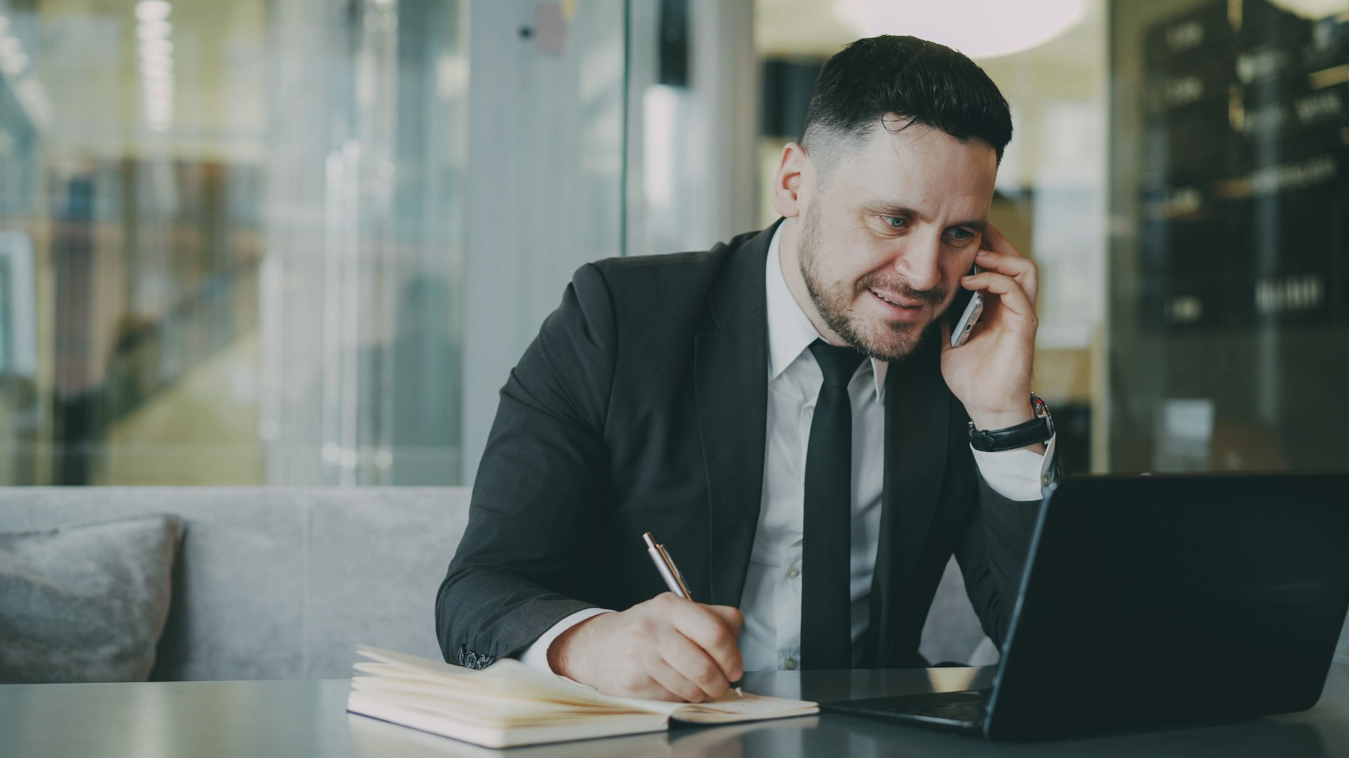 Property manager talking on the phone and taking notes on a laptop in a modern office