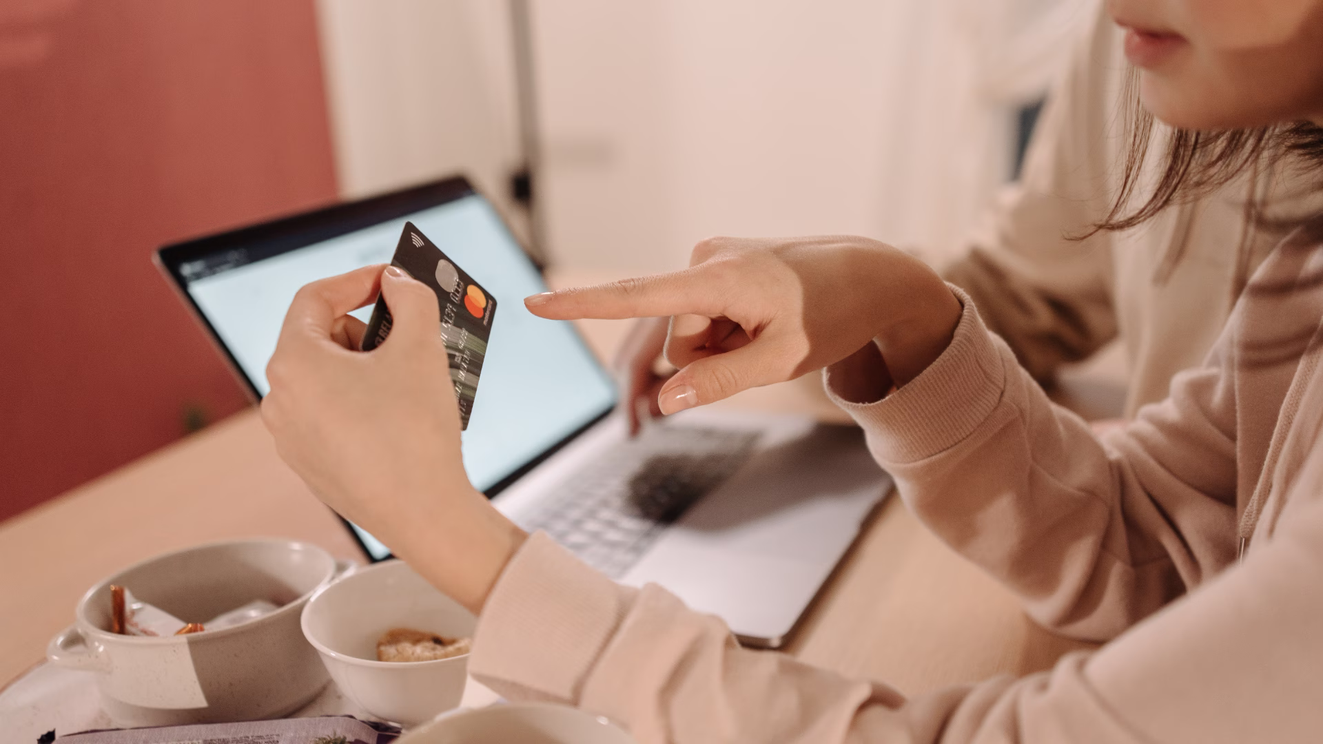 Person using laptop at kitchen table with ID card and phone