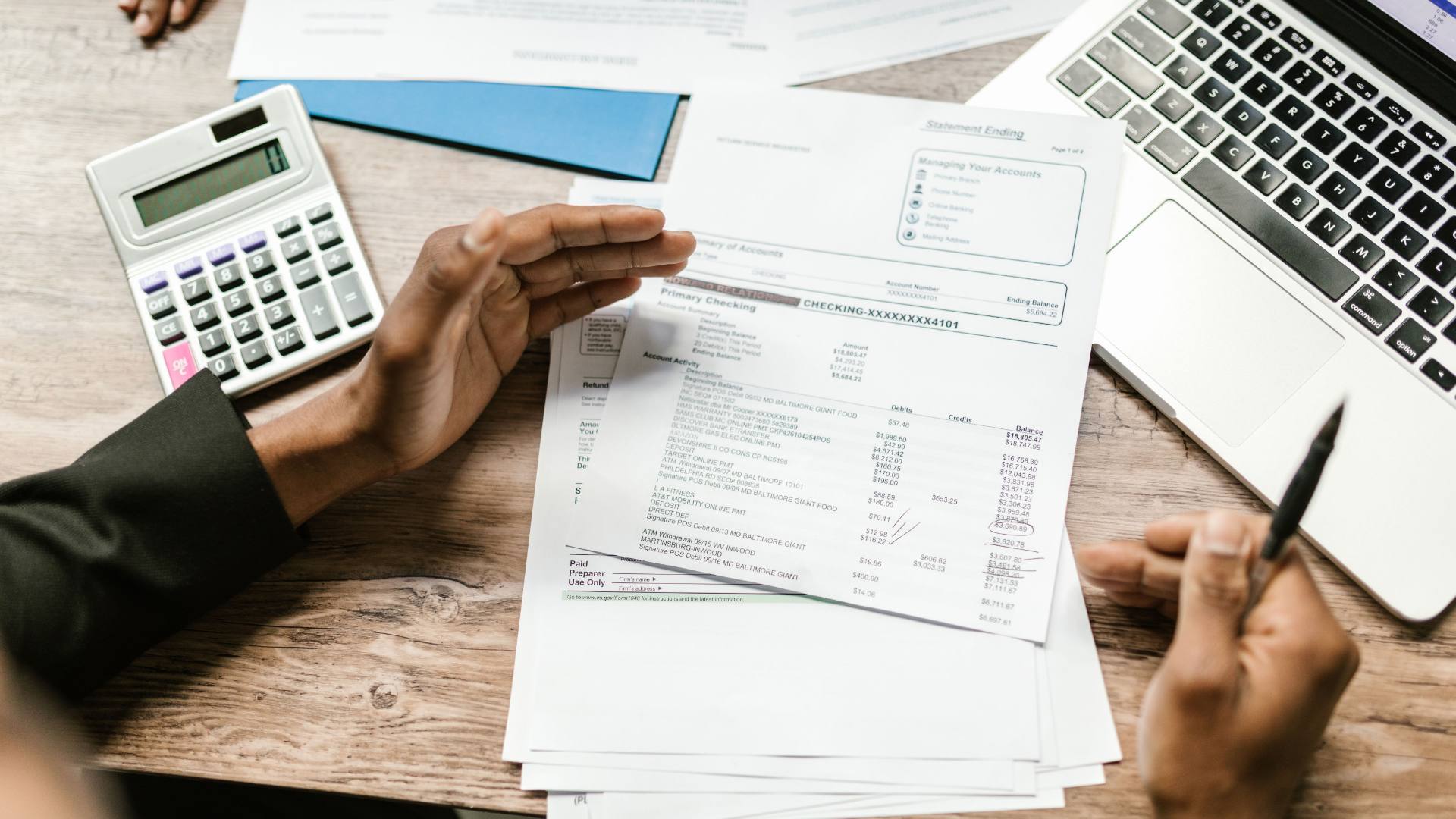 Hands reviewing a financial statement beside a calculator and laptop.