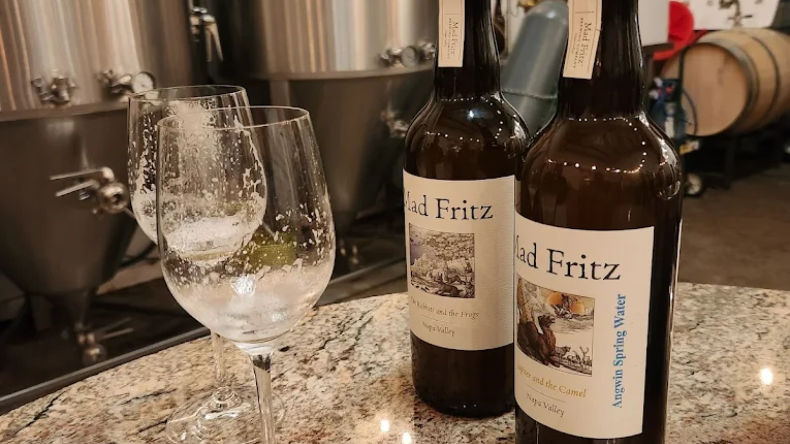 Mad Fritz beer bottles and glasse on a counter in front of tanks and barrels
