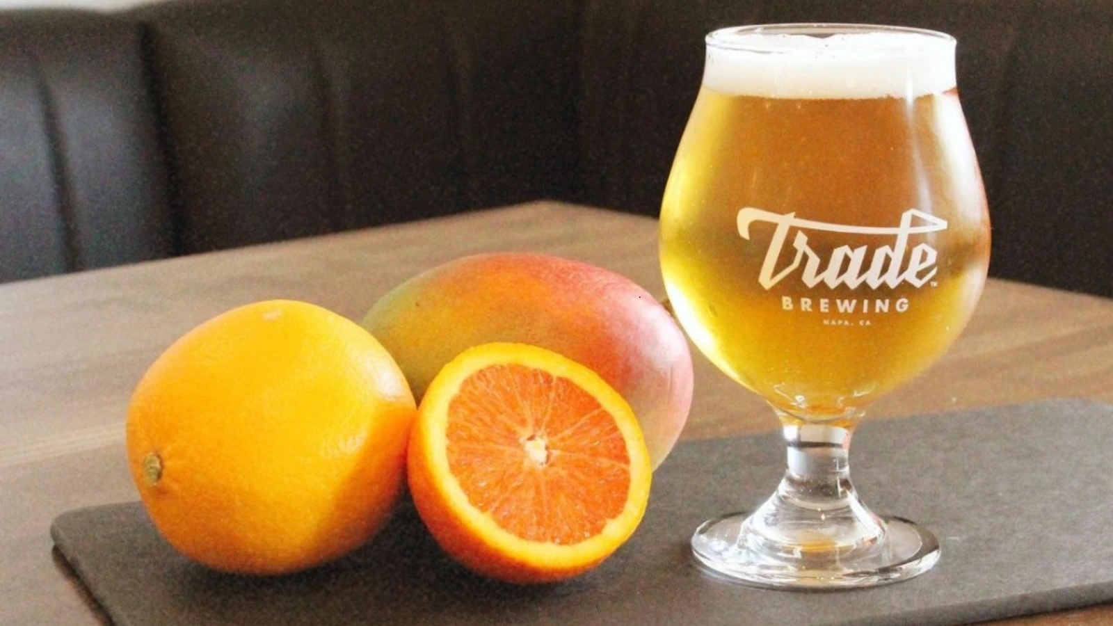 A glass of trade brewing beer next to oranges and a mango