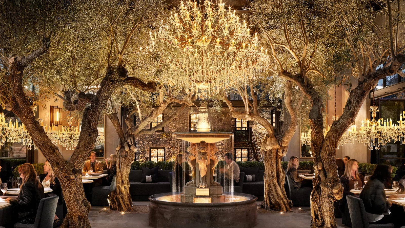 RH Yountville Restaurant features a breathtaking dining room with ancient olive trees growing through the space, illuminated by magnificent crystal chandeliers, and centered around an elegant glass-enclosed display creating an enchanting indoor garden atmosphere