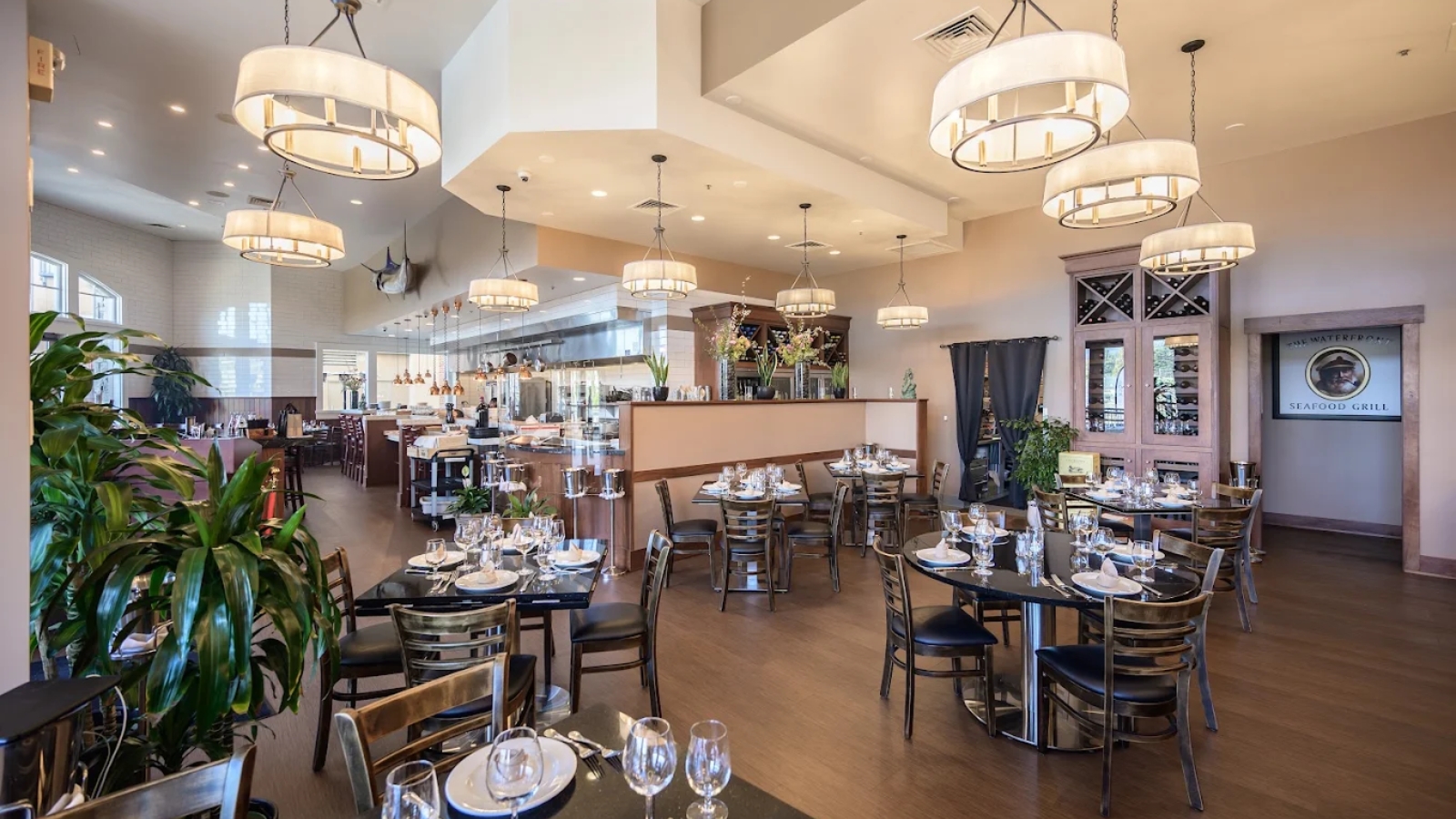 Elegant dining room at Waterfront Grill with set tables, modern lighting, and an open kitchen view.