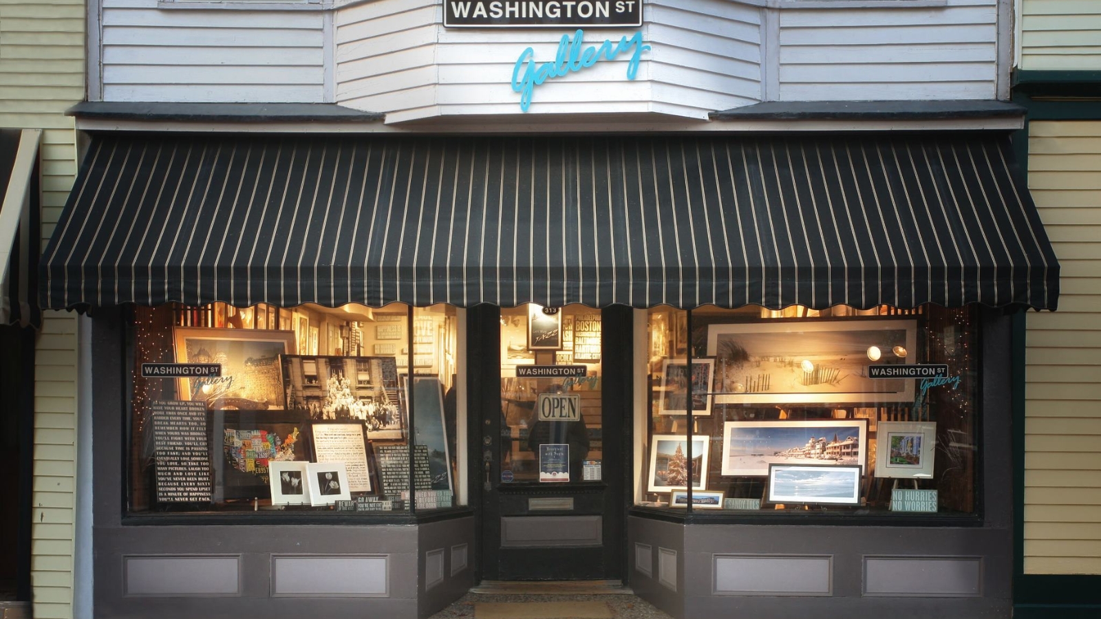 Charming storefront of Washington Street's Galleries featuring large display windows showcasing local artwork, historical photographs, and cultural exhibits under a traditional striped awning in a historic downtown setting.