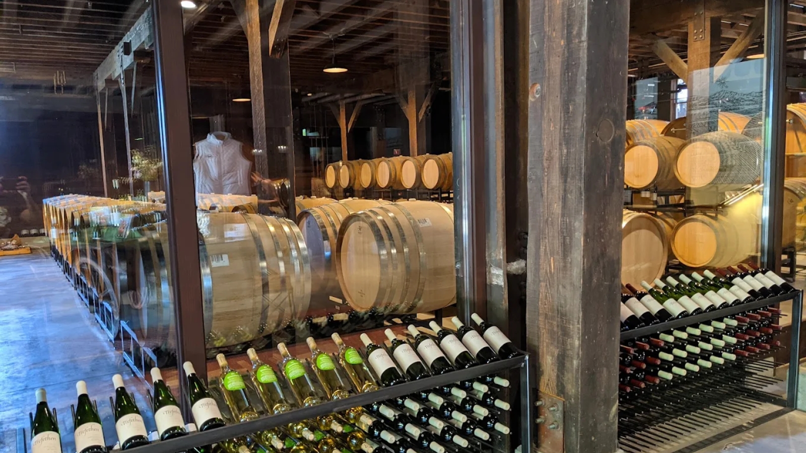 Interior wine cellar at Trefethen Family Vineyards showcasing organized bottle storage racks filled with wines alongside traditional wooden aging barrels under rustic exposed beam architecture in the historic winery facility.