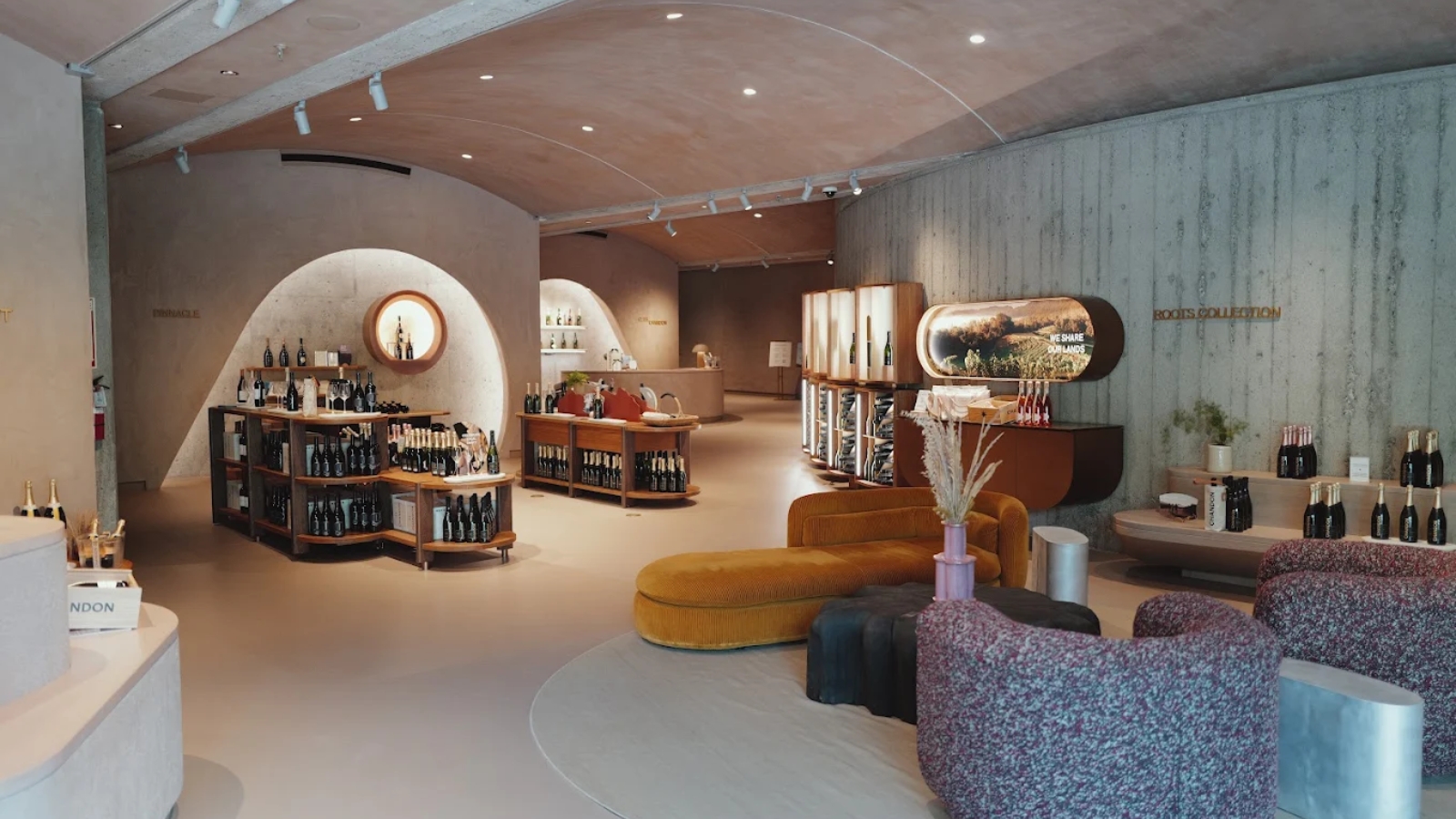 Ultra-modern interior of Chandon winery featuring curved architectural elements, contemporary seating areas, extensive wine displays along curved walls, and a sophisticated retail space with warm lighting creating an upscale sparkling wine tasting experience.