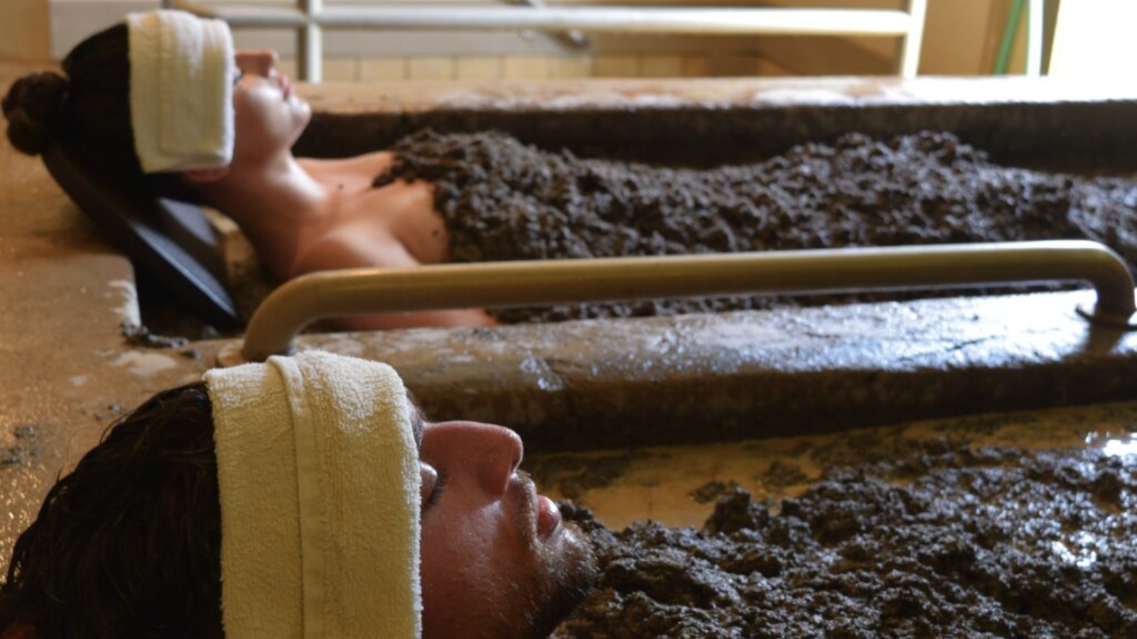 Two guests relaxing in therapeutic volcanic mud bath tubs at Golden Haven Hot Springs mud baths in Calistoga, with white towels covering their faces during the mineral-rich spa treatment.